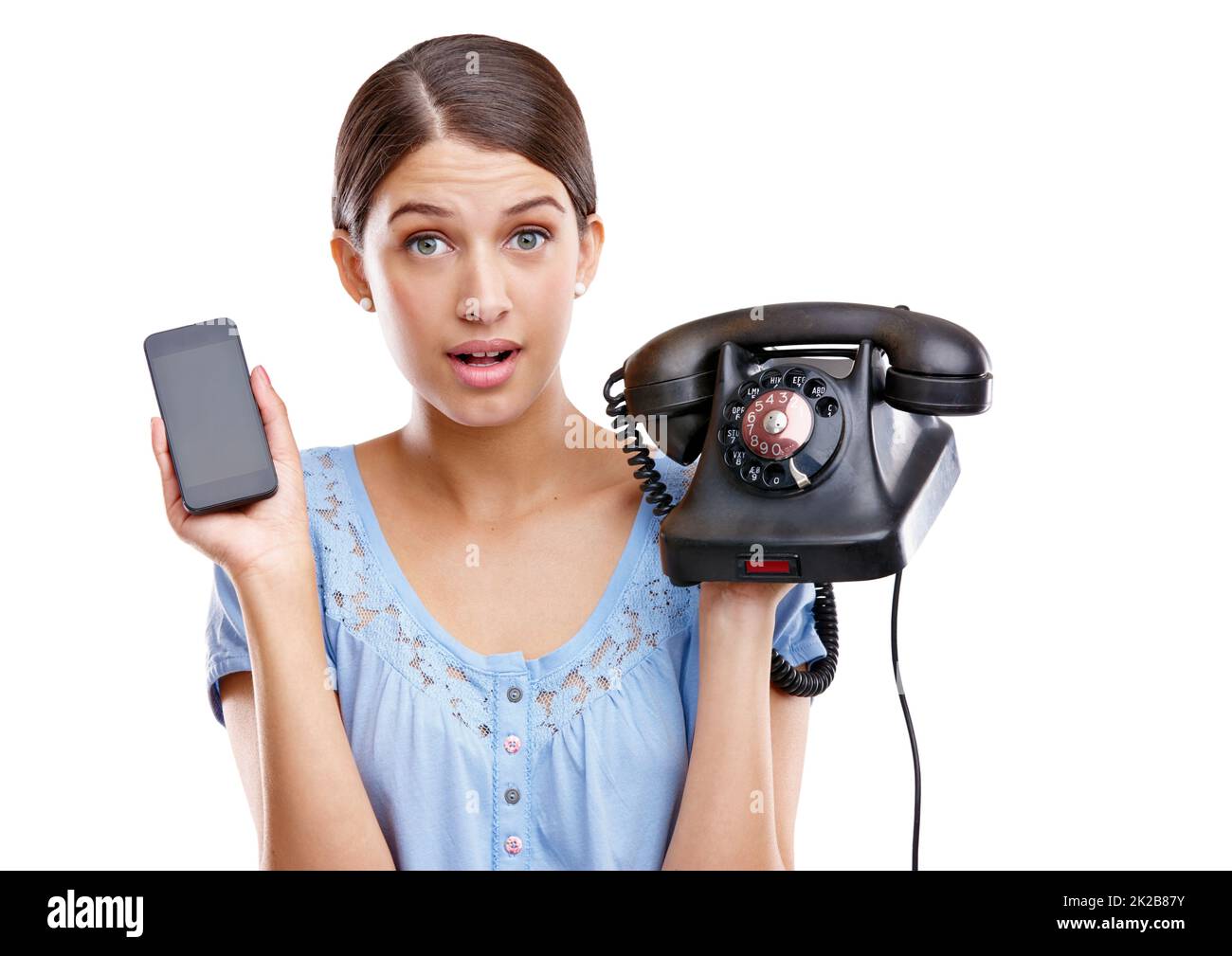 Call us for more information. A young woman holding a mobile phone in one hand and an old-fashioned phone in the other. Stock Photo