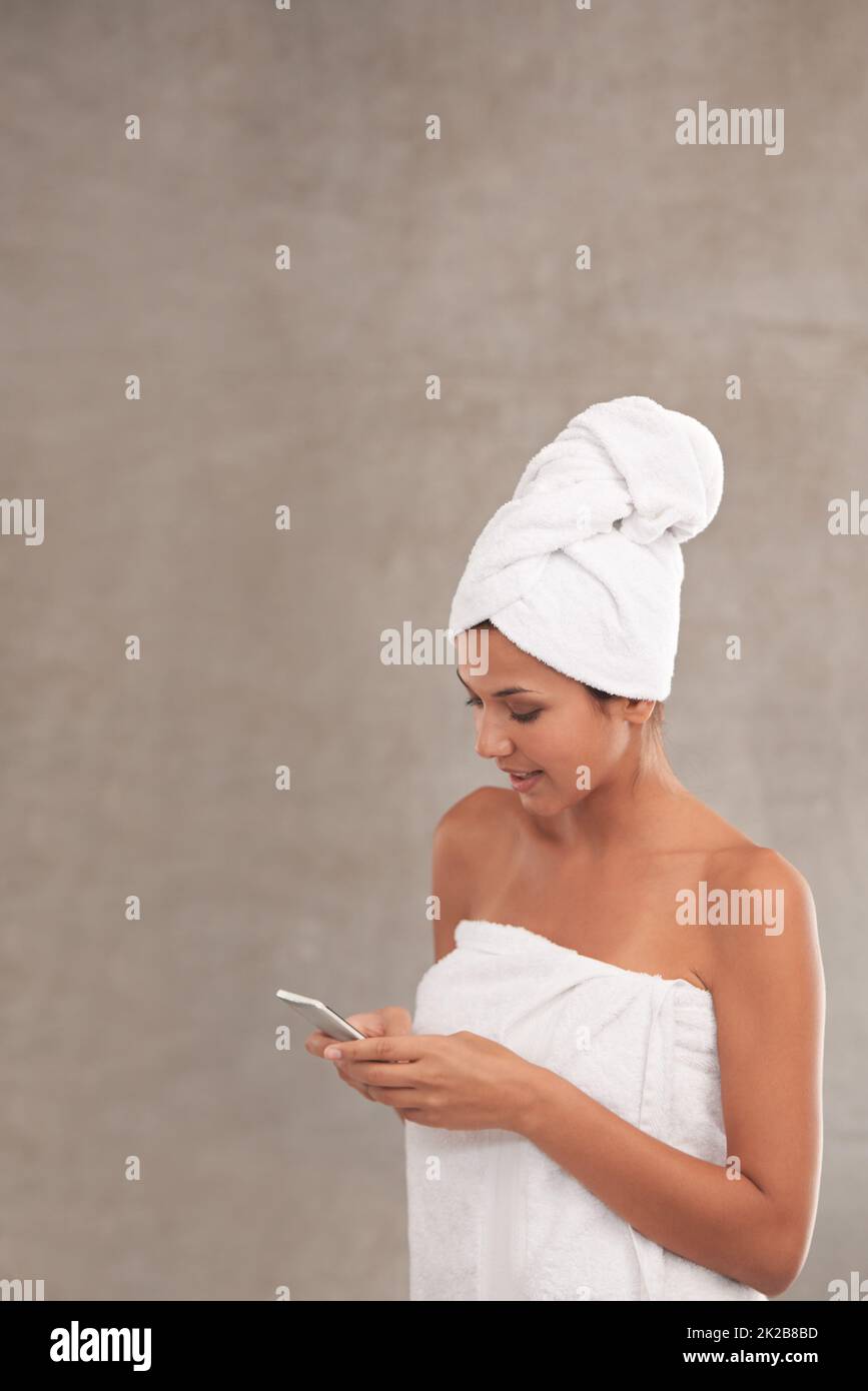 Catching up on the morning gossip. A beautiful young woman in a towel texting in her bathroom. Stock Photo