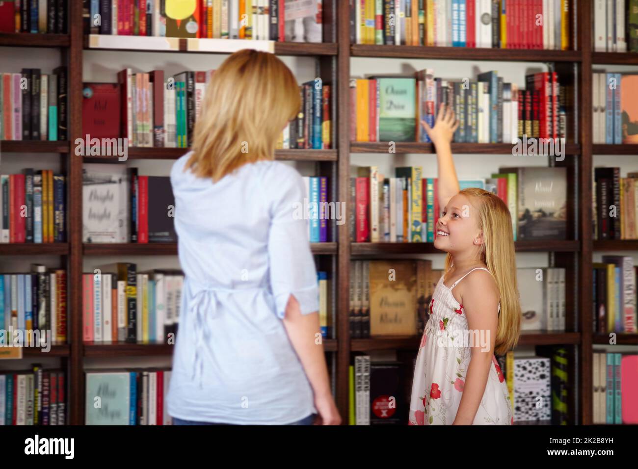 I love books. Young blond girl reaching for a book in the library. Stock Photo