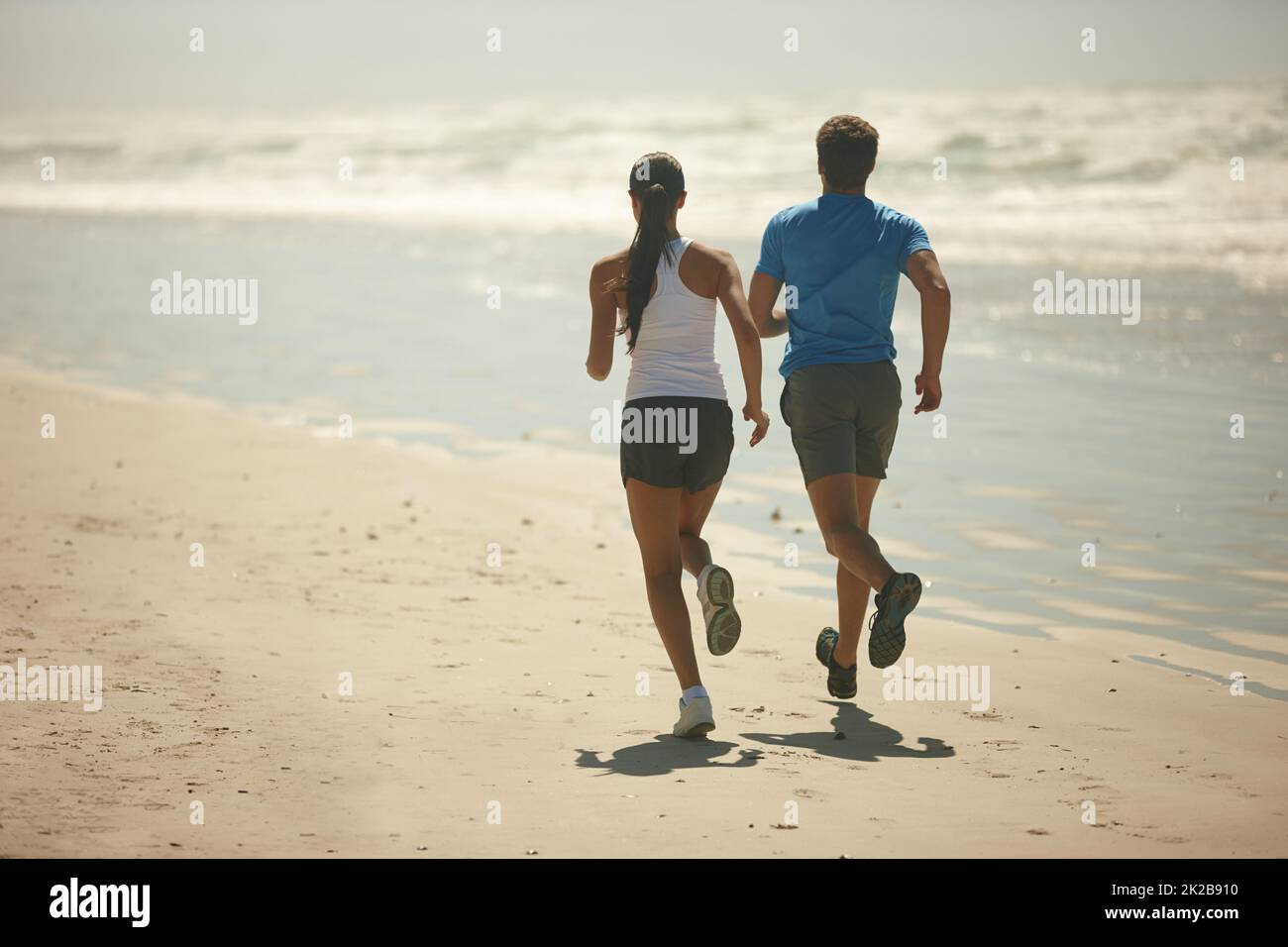 There are no shortcuts to any place worth going. Rearview shot of a young couple jogging together on the beach. Stock Photo