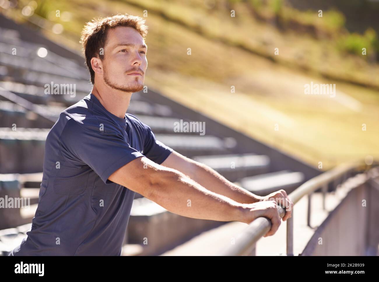 Great day to be at the track. Shot of a handsome young man stretching at an athletics arena. Stock Photo