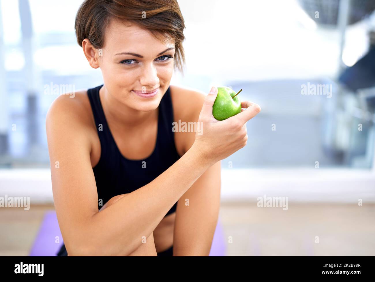 All part of the healthy lifestyle. Shot of a sporty young woman sitting on a gym floor eating an apple. Stock Photo