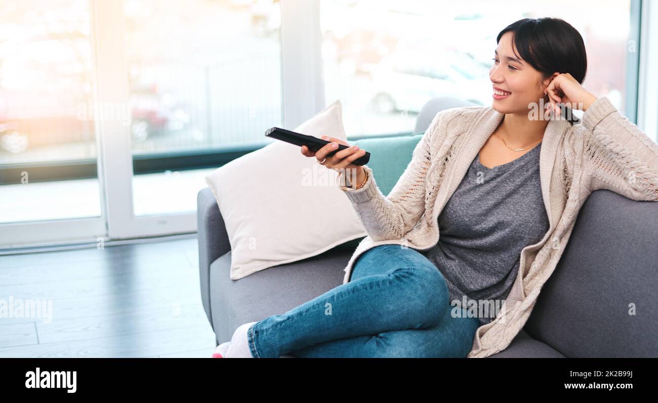 Whats on the TV. Shot of a cheerful young woman holding a remote to