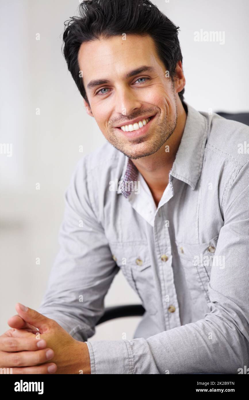 A confident smile makes everything worthwhile. Shot of a handsome young sitting in a chair. Stock Photo