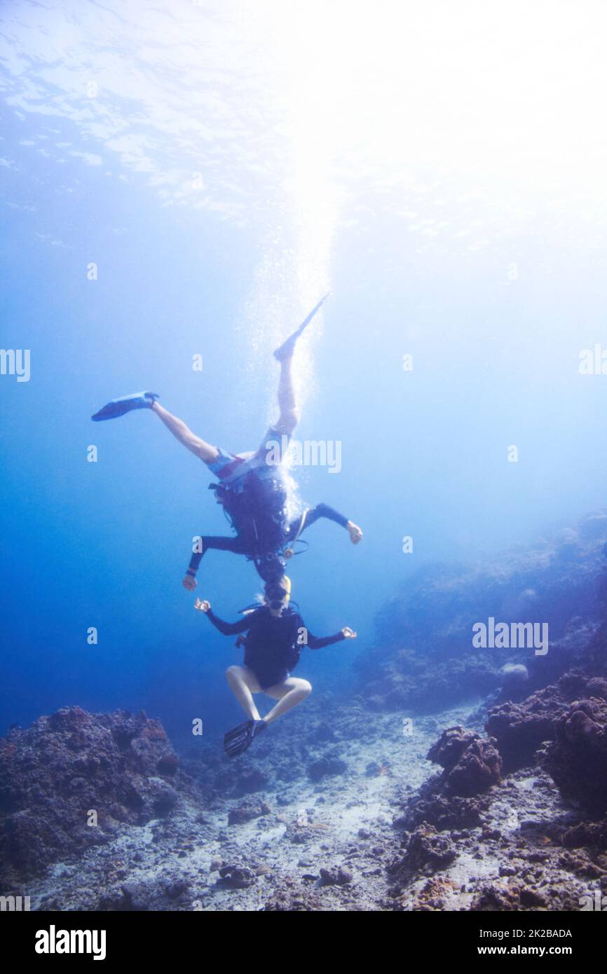 Underwater escapades. Two buoyant scuba divers fooling around underwater head to head and upside down - Copyspace. Stock Photo