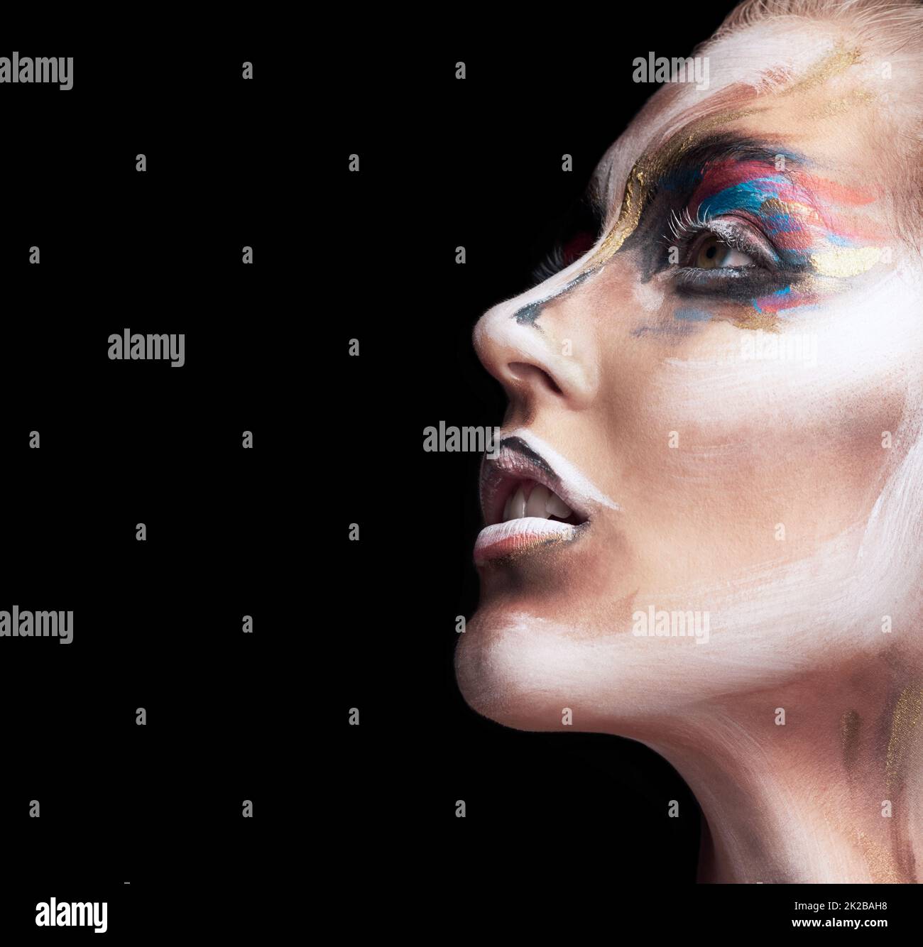 Closeup in colour. Studio shot of a young woman posing with paint on her face isolated on black. Stock Photo