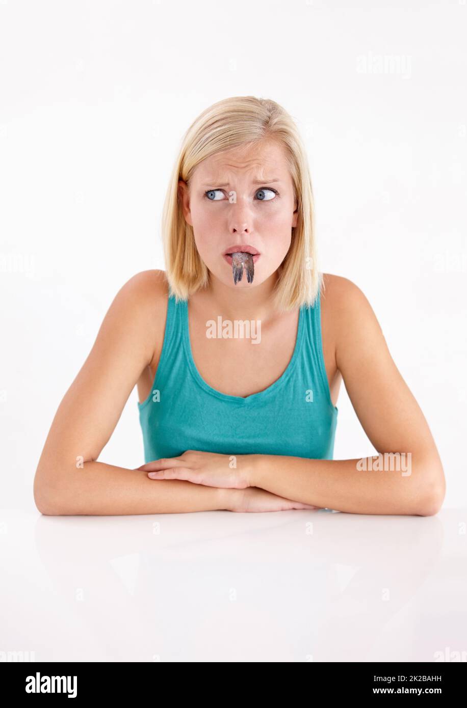 Ill eat it if I have to. A young woman pulling a face with a fish in her mouth. Stock Photo
