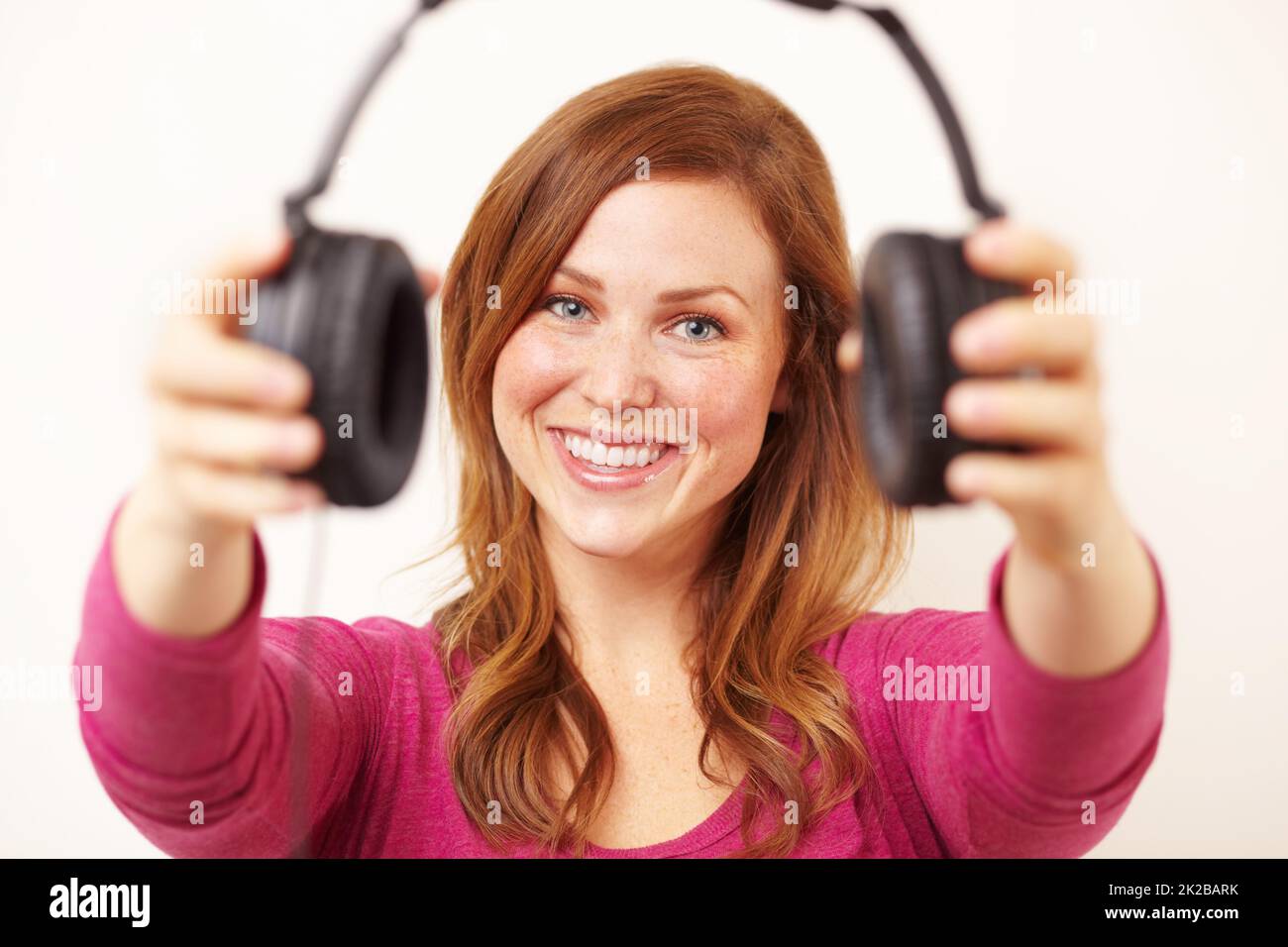 Hear, have a listen to this. Portrait of an attractive young woman offering you a pair of headphones. Stock Photo