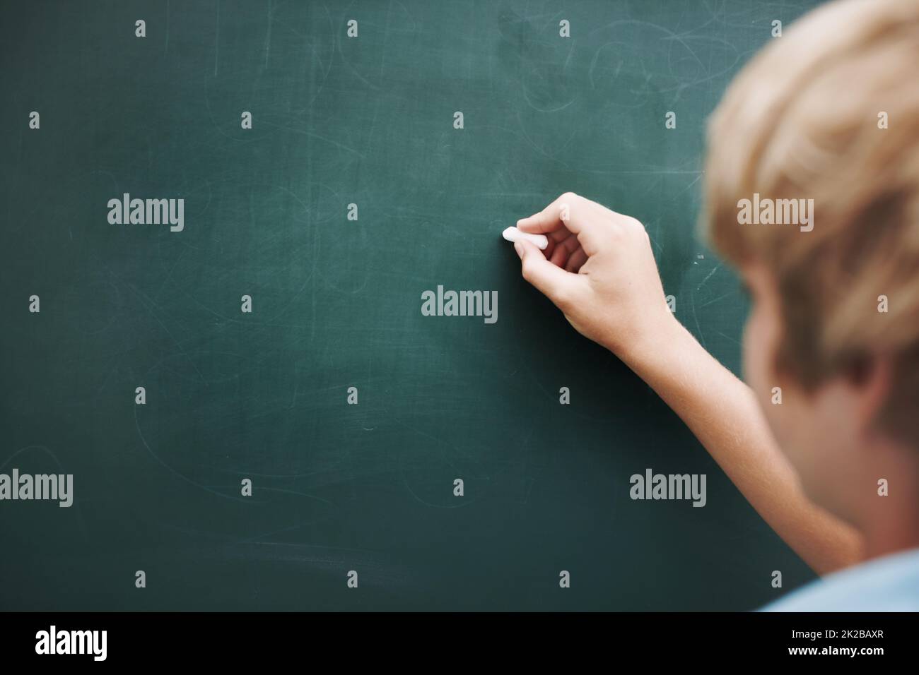 Hes writing your copy or you. Rear view of a young boy writing something on a blackboard with a piece of chalk - copyspace. Stock Photo