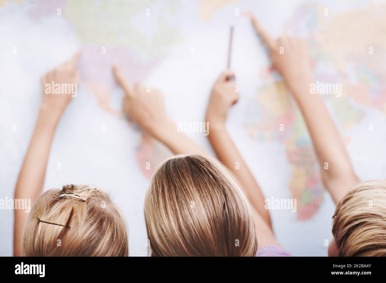 There are so many places to visit. Rear view of a group of schoolchildren pointing at a world map. Stock Photo