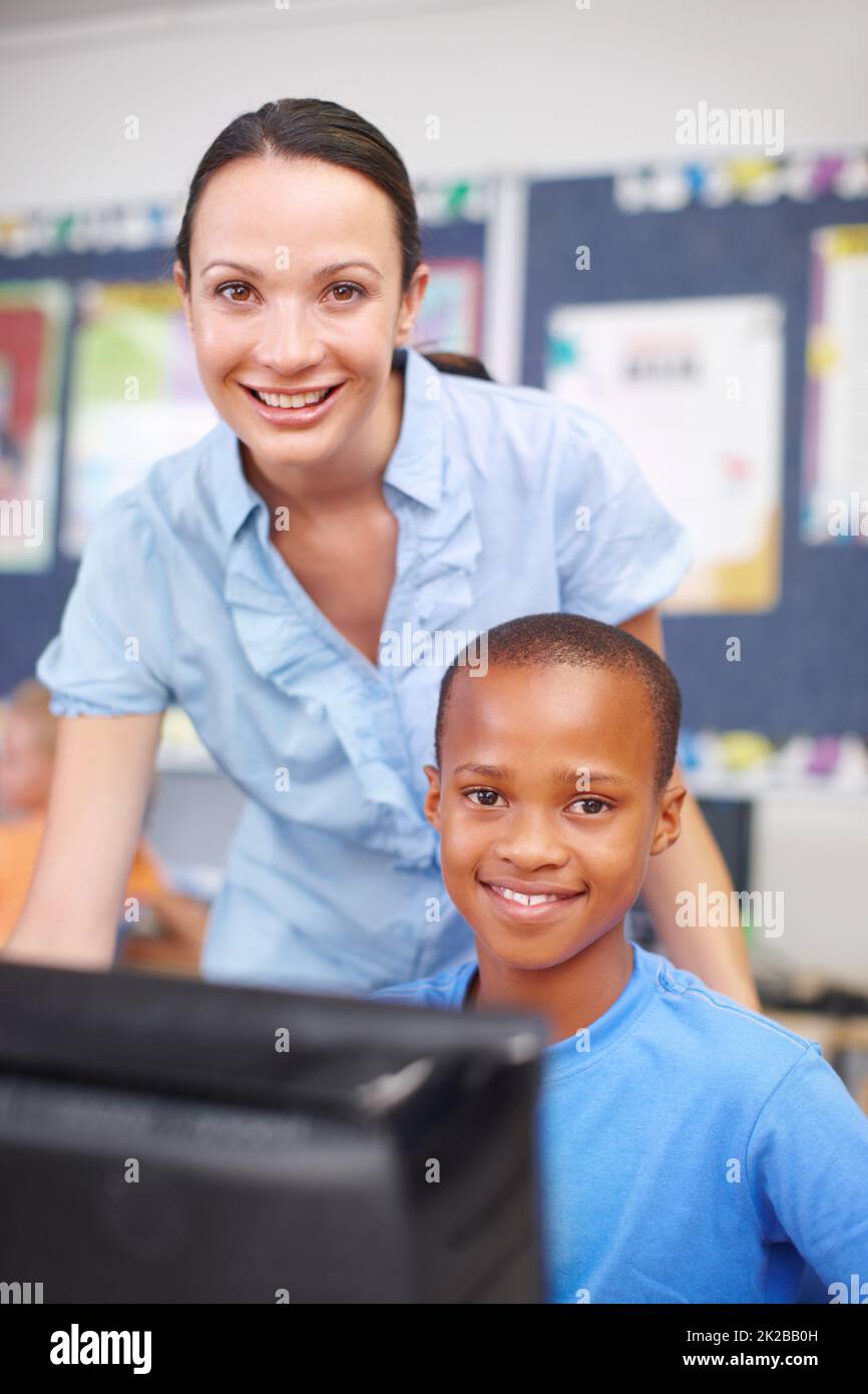 He could have a bright future in IT. Portrait of a beautiful young woman helping out a young ethnic boy in computer class. Stock Photo