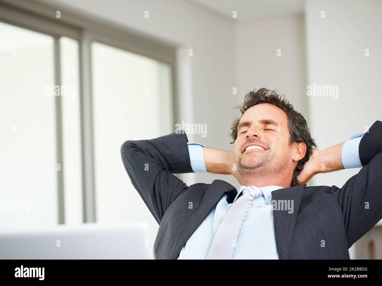 Relaxed executive using laptop. Smart mature business man using laptop and relaxing with hands behind head. Stock Photo