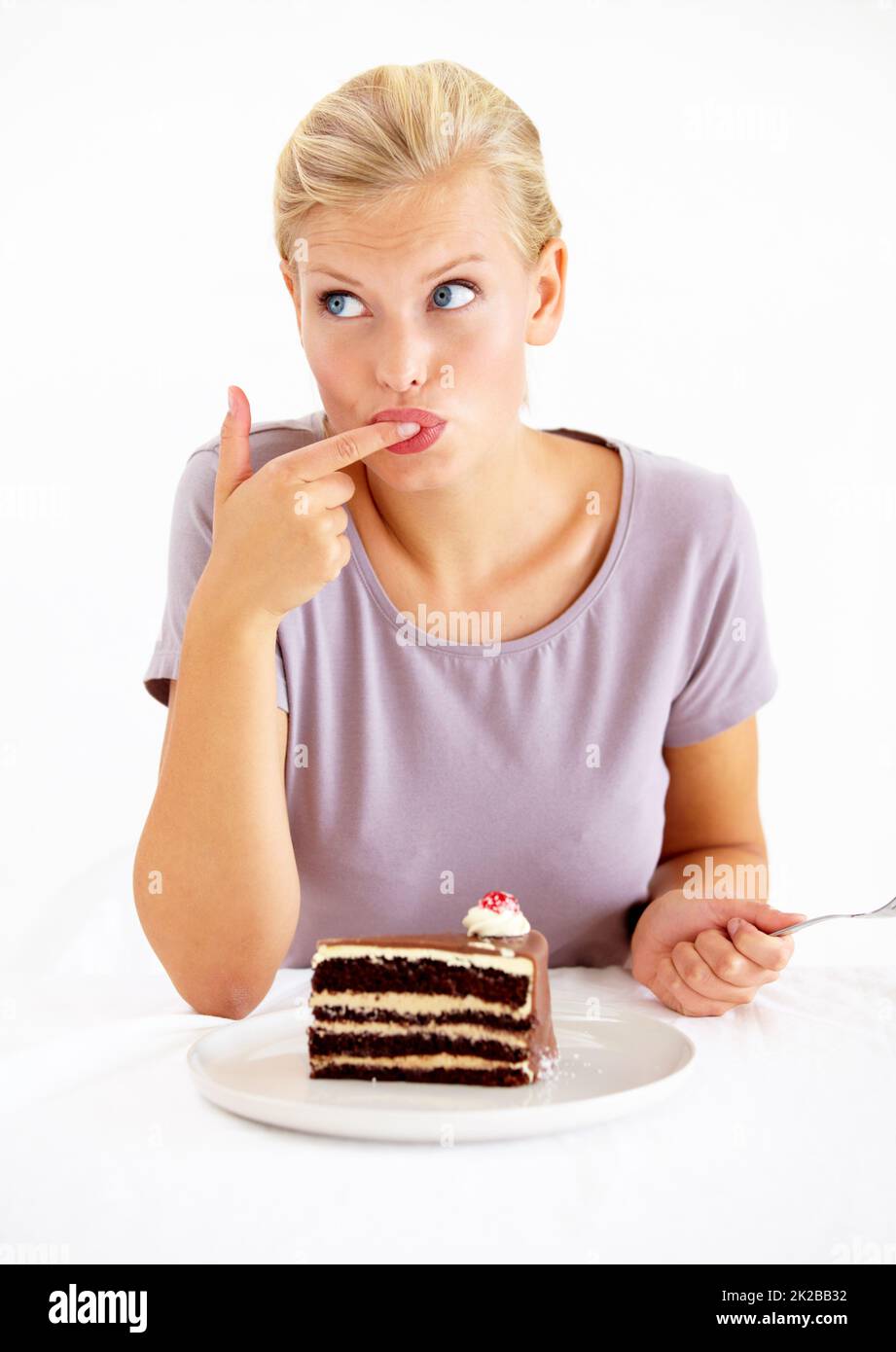 Trying a small taste.... Young woman tasting the frosting of a delicious piece of chocolate cake. Stock Photo