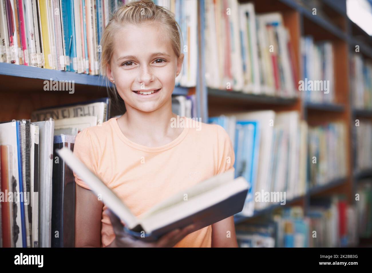Ill be a writer one day. Portrait of a cute young girl reading a book in the library. Stock Photo