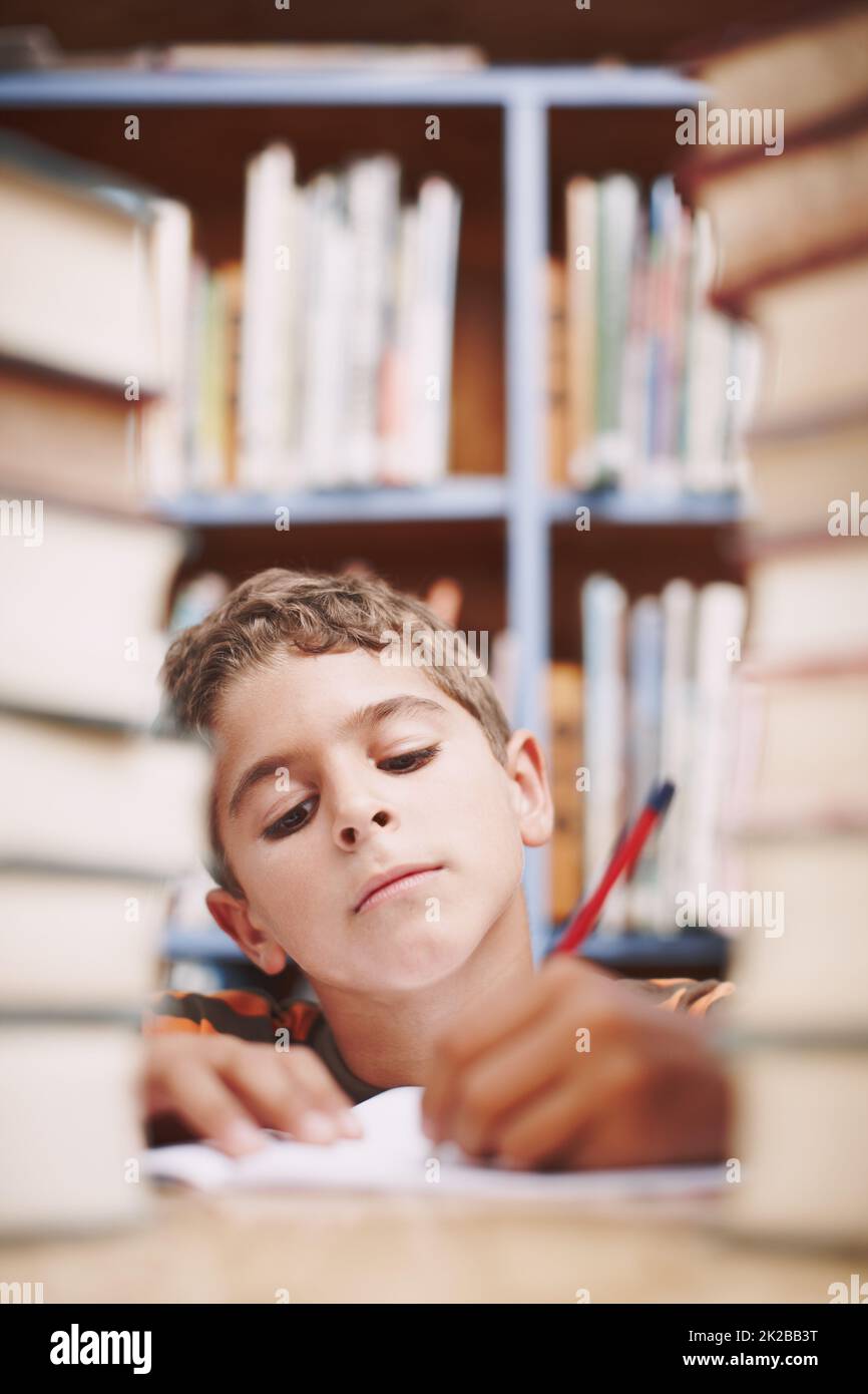Hmmm.... A young boy doing some creative writing between a stack of books. Stock Photo