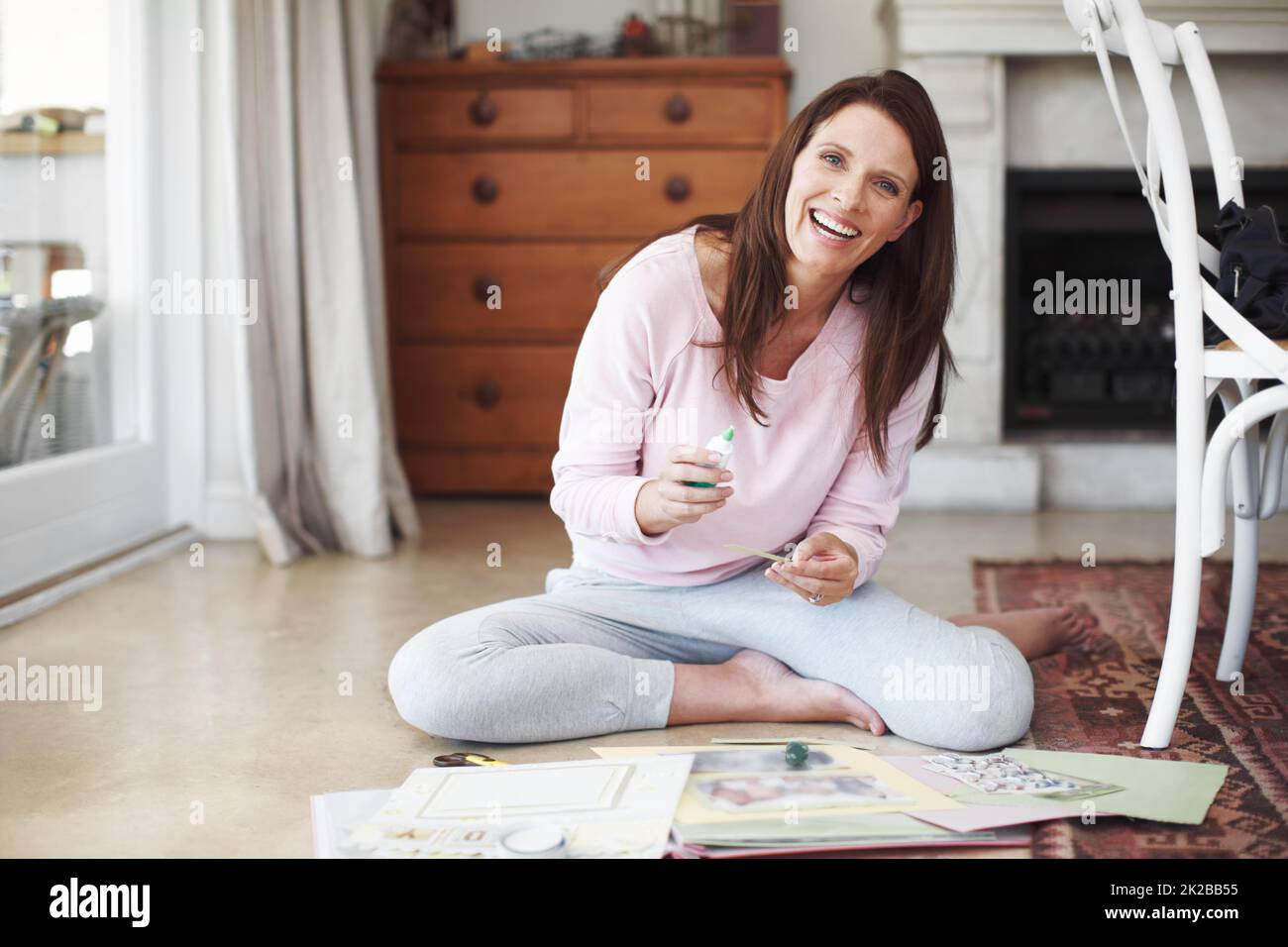Shes enjoying her new hobby. A smiling woman working on a scrapbook while sitting on the floor in a home interior. Stock Photo
