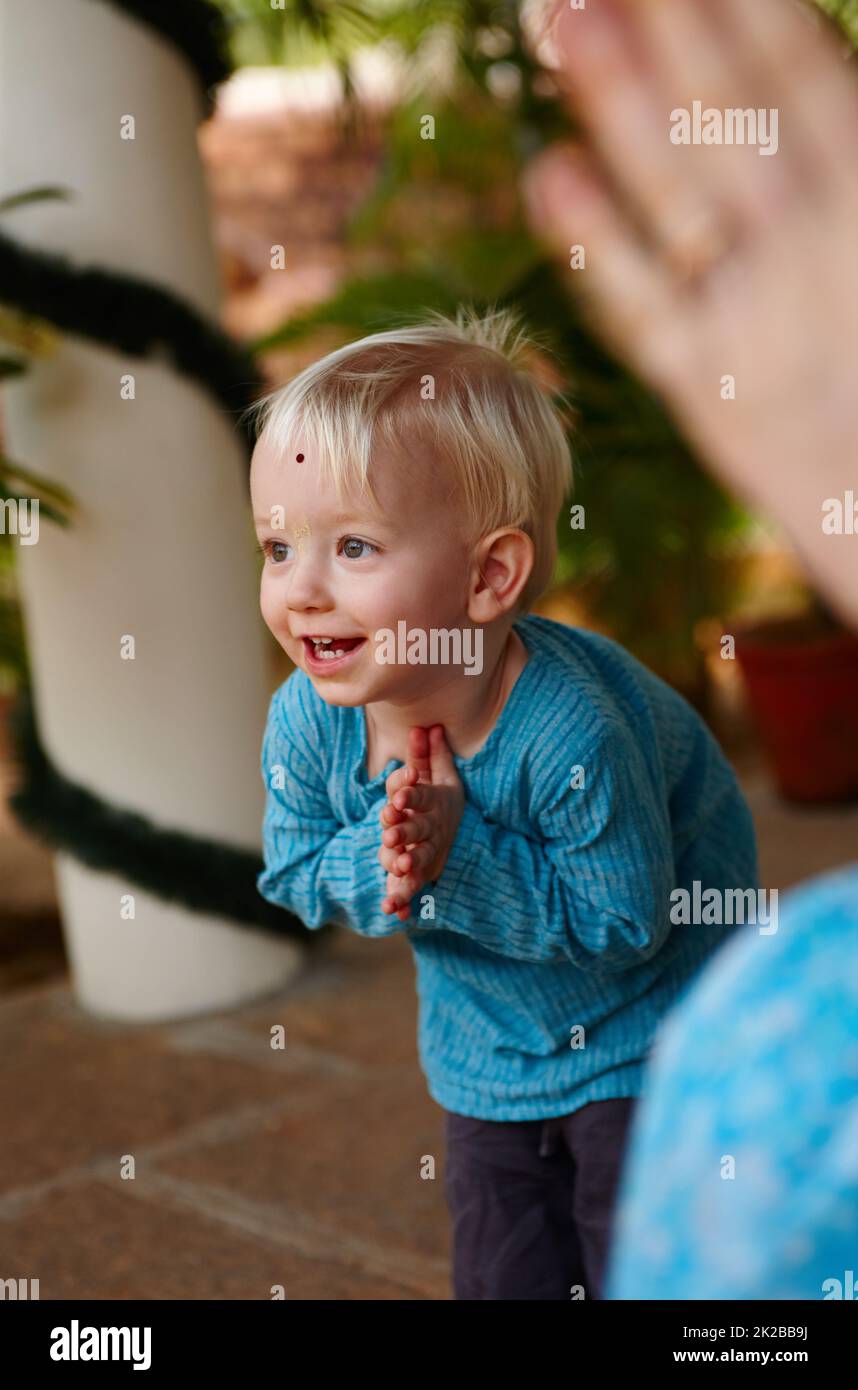Learning the ways of tradition. Cute little boy adorned with a bindi on his forehead, bowing in a Hindu temple. Stock Photo