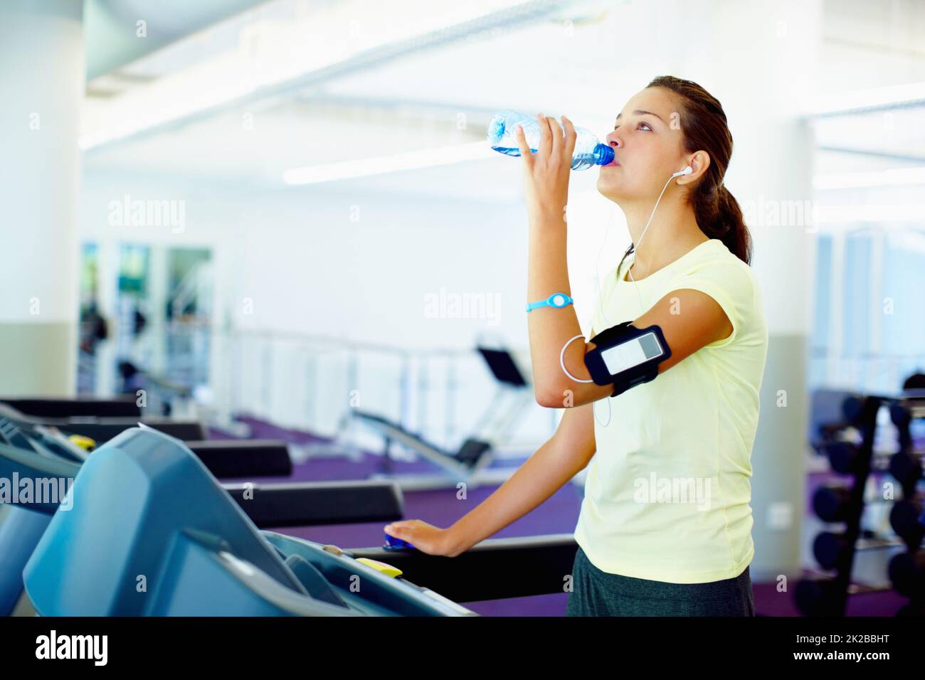 Young woman drinking water. Young woman standing on treadmill and