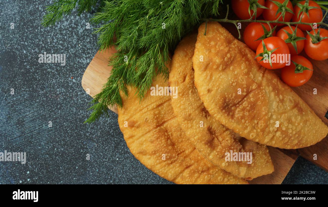 Cheburek with meat and cherry tomatoes. Traditional Romania, Ukrainian, Russian and Tatar food National east meal. Meat pie  with beef, veal or lamb Stock Photo