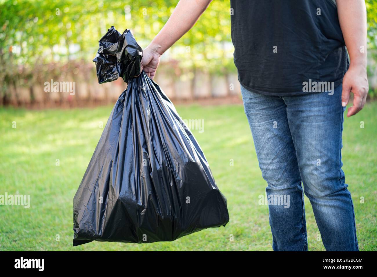 Woman holding black plastic trash bin bags of garbage on the pavement, clean environment concept. Stock Photo