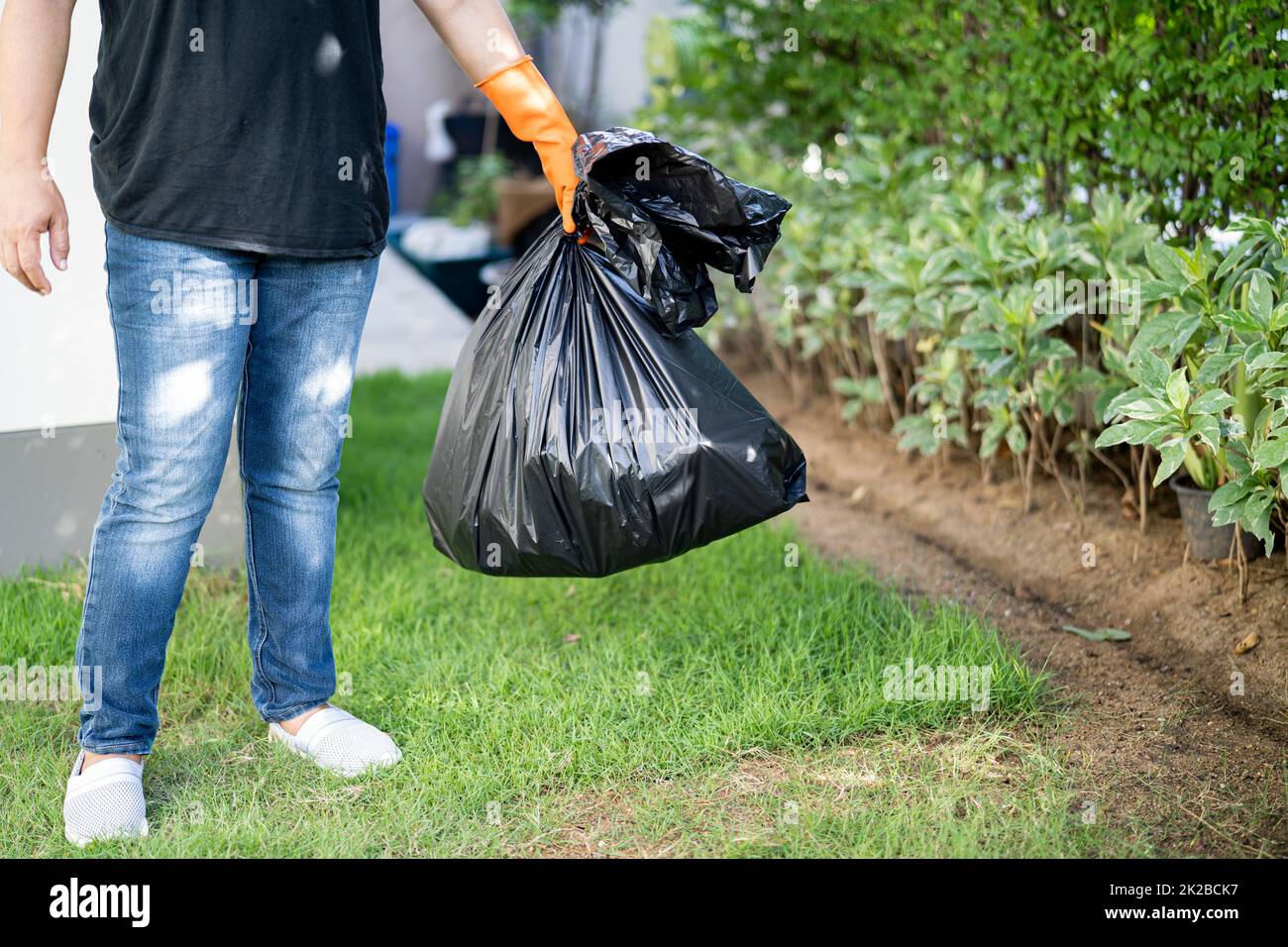 Woman holding black plastic trash bin bags of garbage on the pavement