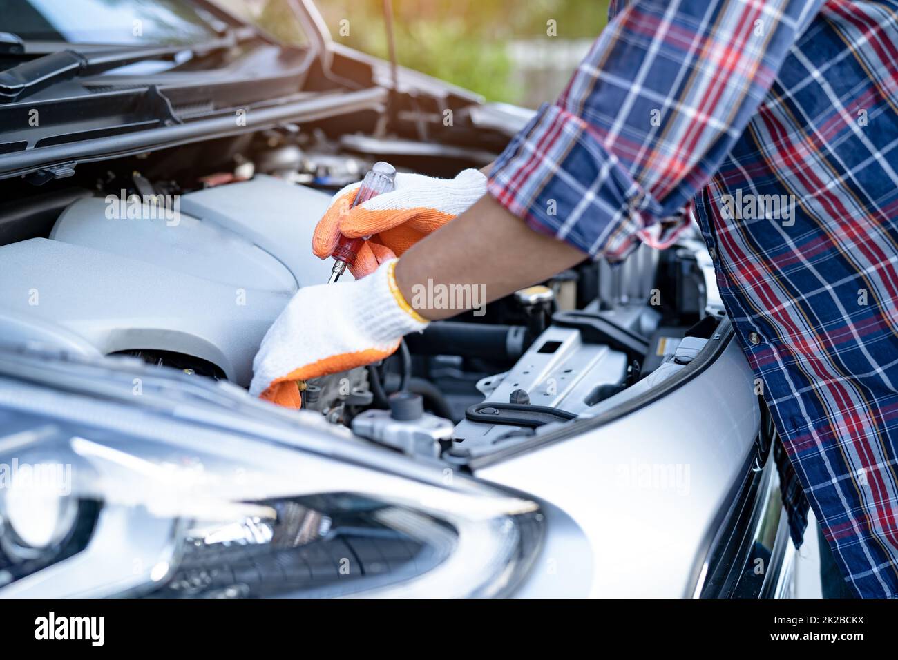 Asian auto mechanic check for repair under the hood of broken down car