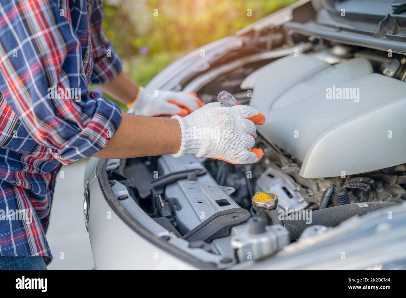 Asian auto mechanic check for repair under the hood of broken down car