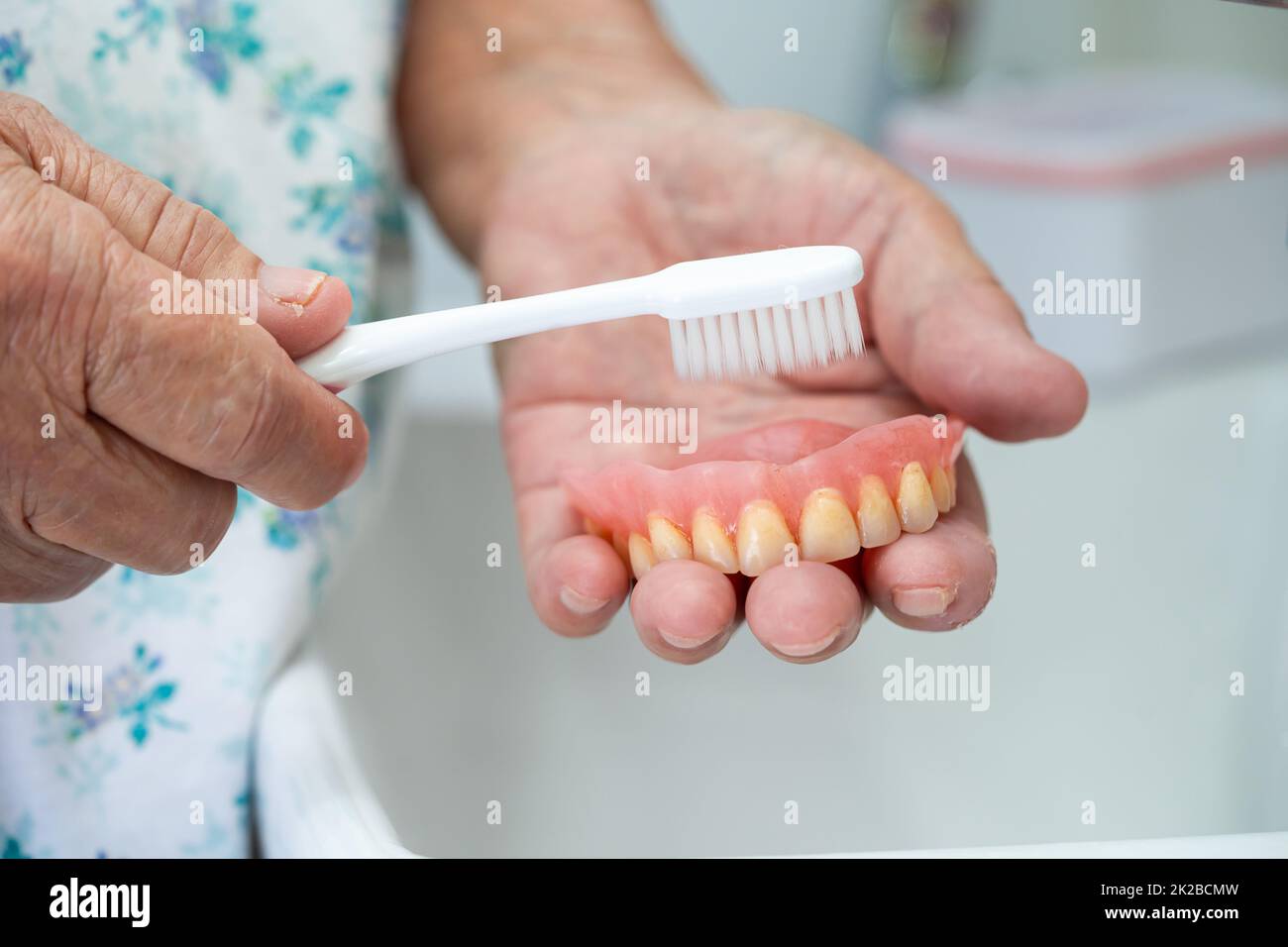 Asian senior or elderly old woman patient use toothbrush to clean partial denture of replacement teeth. Stock Photo