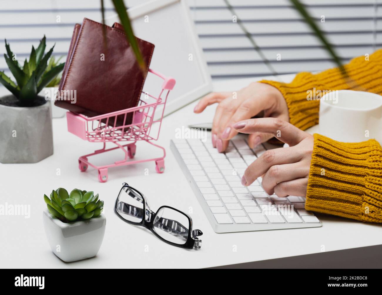 woman in an orange sweater sits at a table and works at a computer. Remote work, freelance. Online shopping Stock Photo