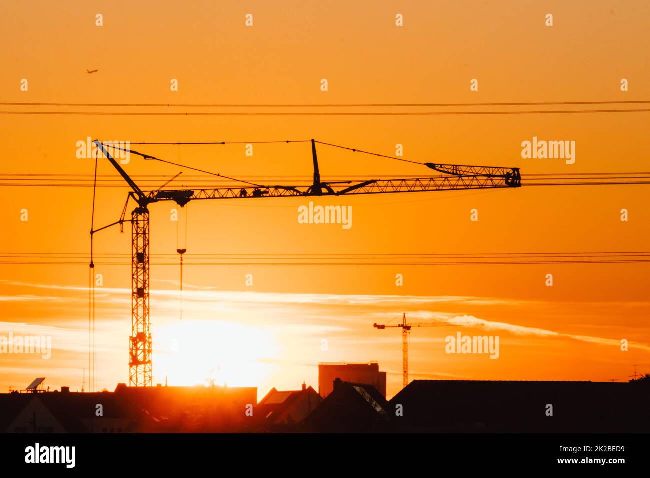 Tall construction crane silhouette in orange sky sunset shows construction site with engineering for modern buildings and city development as architectural teamwork for skyscrapers high voltage lines Stock Photo