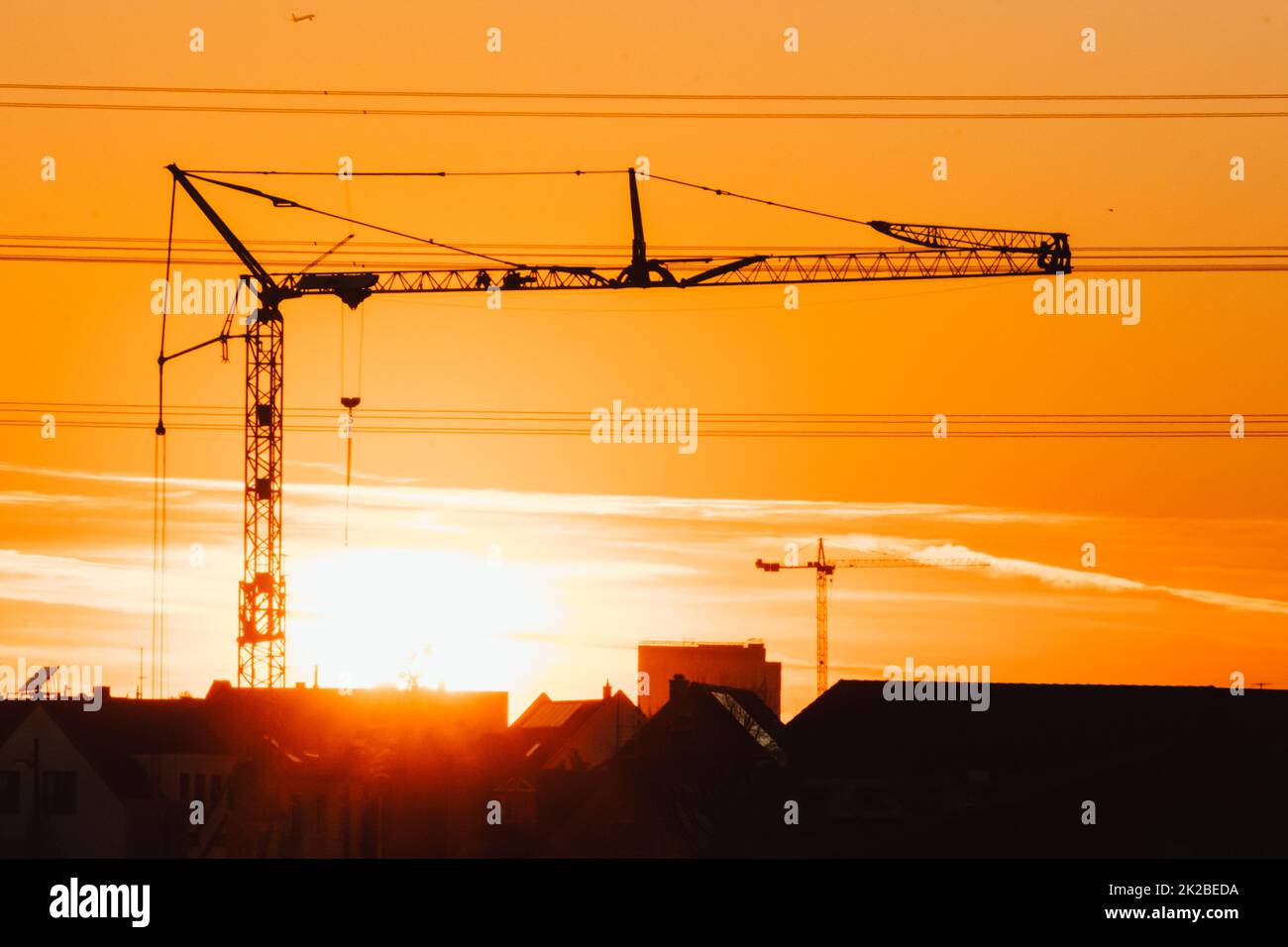 Tall construction crane silhouette in orange sky sunset shows construction site with engineering for modern buildings and city development as architectural teamwork for skyscrapers high voltage lines Stock Photo