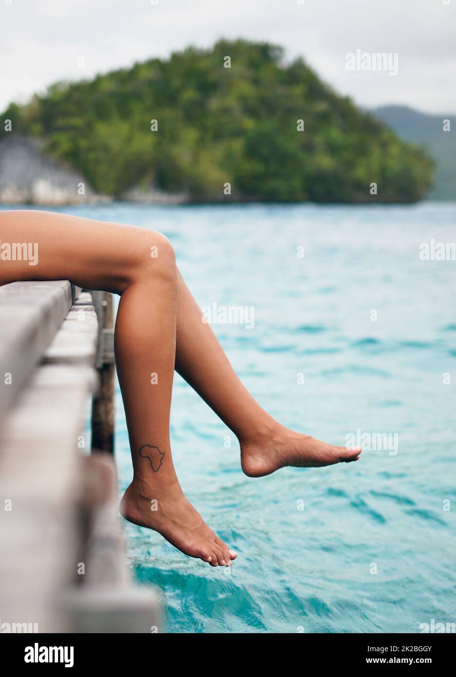 Vacation mode on. Cropped shot of an unrecognizable woman sitting and dangling her legs over the edge of a boardwalk during vacation. Stock Photo