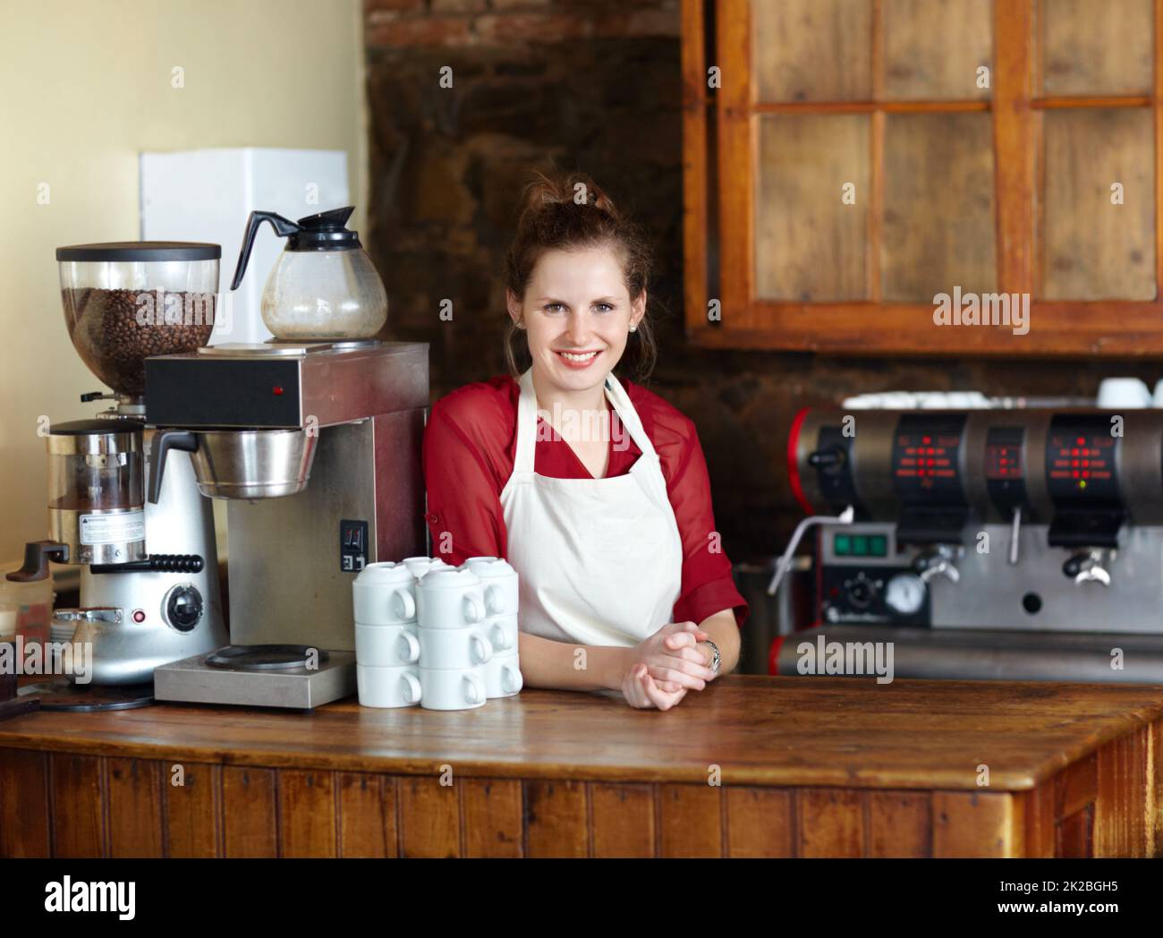 Being a barista is my passion. Pretty young coffee steward behind the counter at work - portrait. Stock Photo