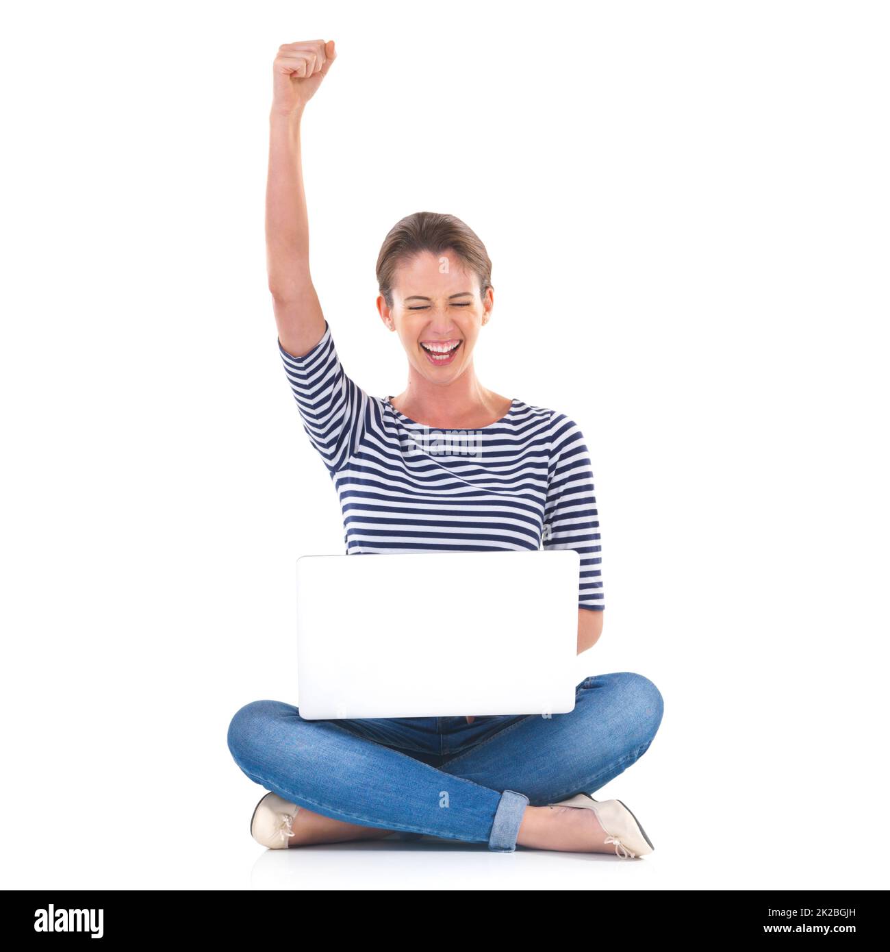 One million likes. Studio shot of a young woman sitting cross legged on the floor cheering while using a laptop. Stock Photo