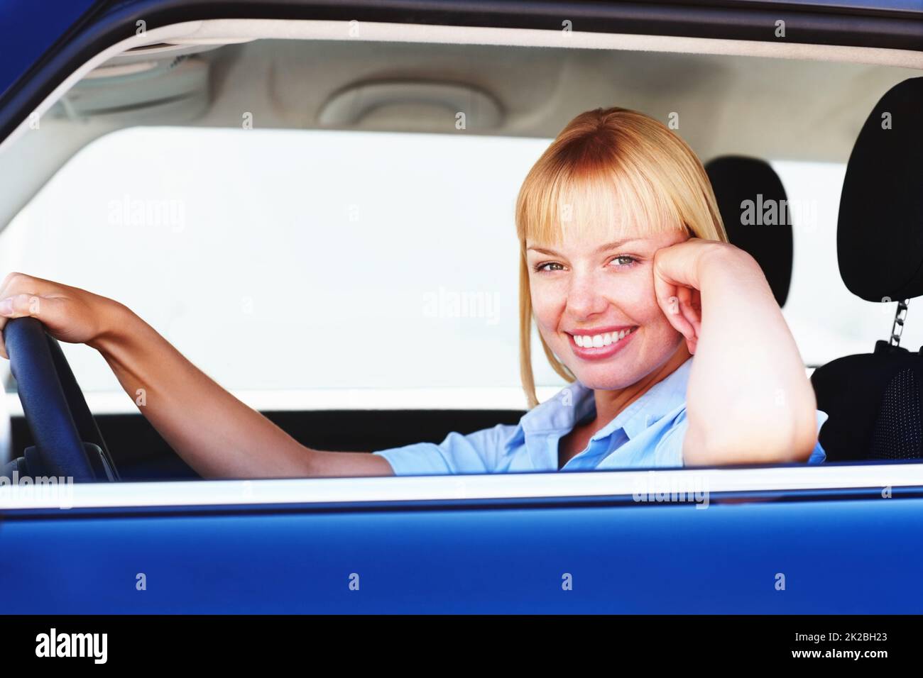 Pretty woman smiling from the drivers seat of a car. Smiling blond woman in a car sitting at the drivers seat. Stock Photo