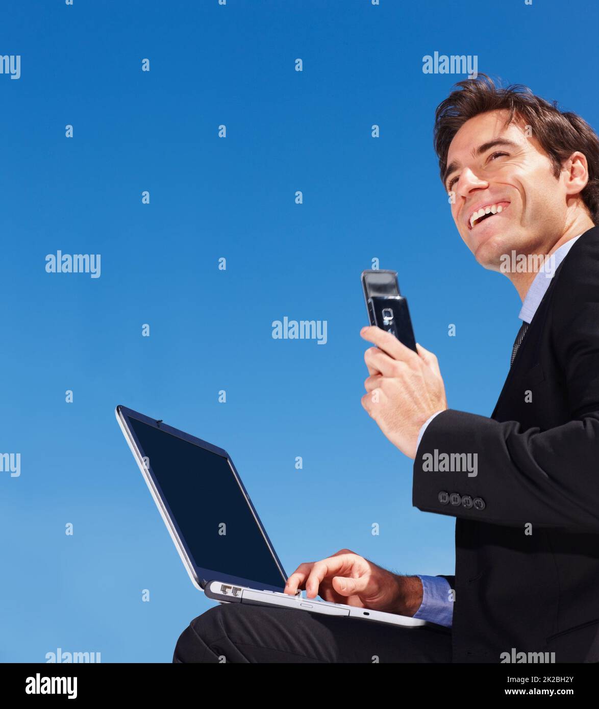 business man using a laptop while holding a mobile phone. Successful young business man using a laptop while holding a mobile phone. Stock Photo