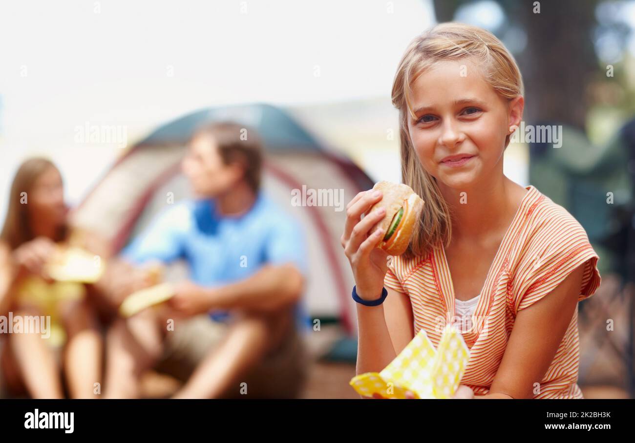 Cute girl eating burger. Portrait of cute young girl eating burger while on a camping holiday with family. Stock Photo