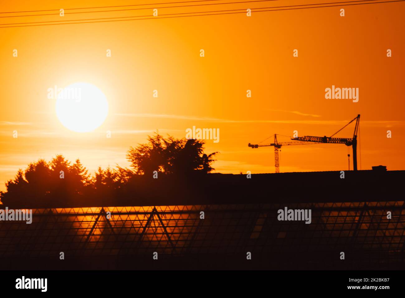 Tall construction crane silhouette in orange sky sunset shows construction site with engineering for modern buildings and city development as architectural teamwork for skyscrapers high voltage lines Stock Photo