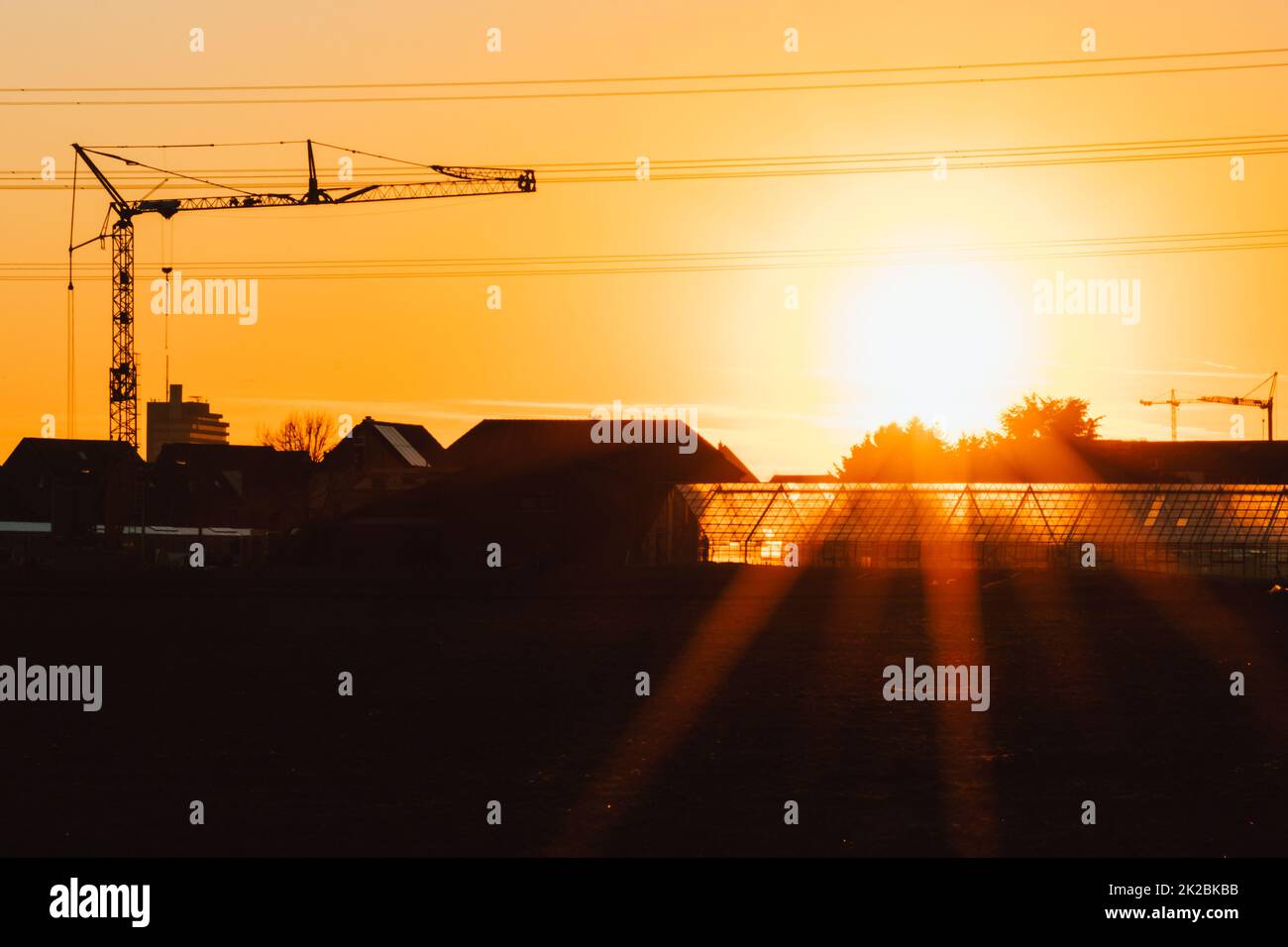 Tall construction crane silhouette in orange sky sunset shows construction site with engineering for modern buildings and city development as architectural teamwork for skyscrapers high voltage lines Stock Photo