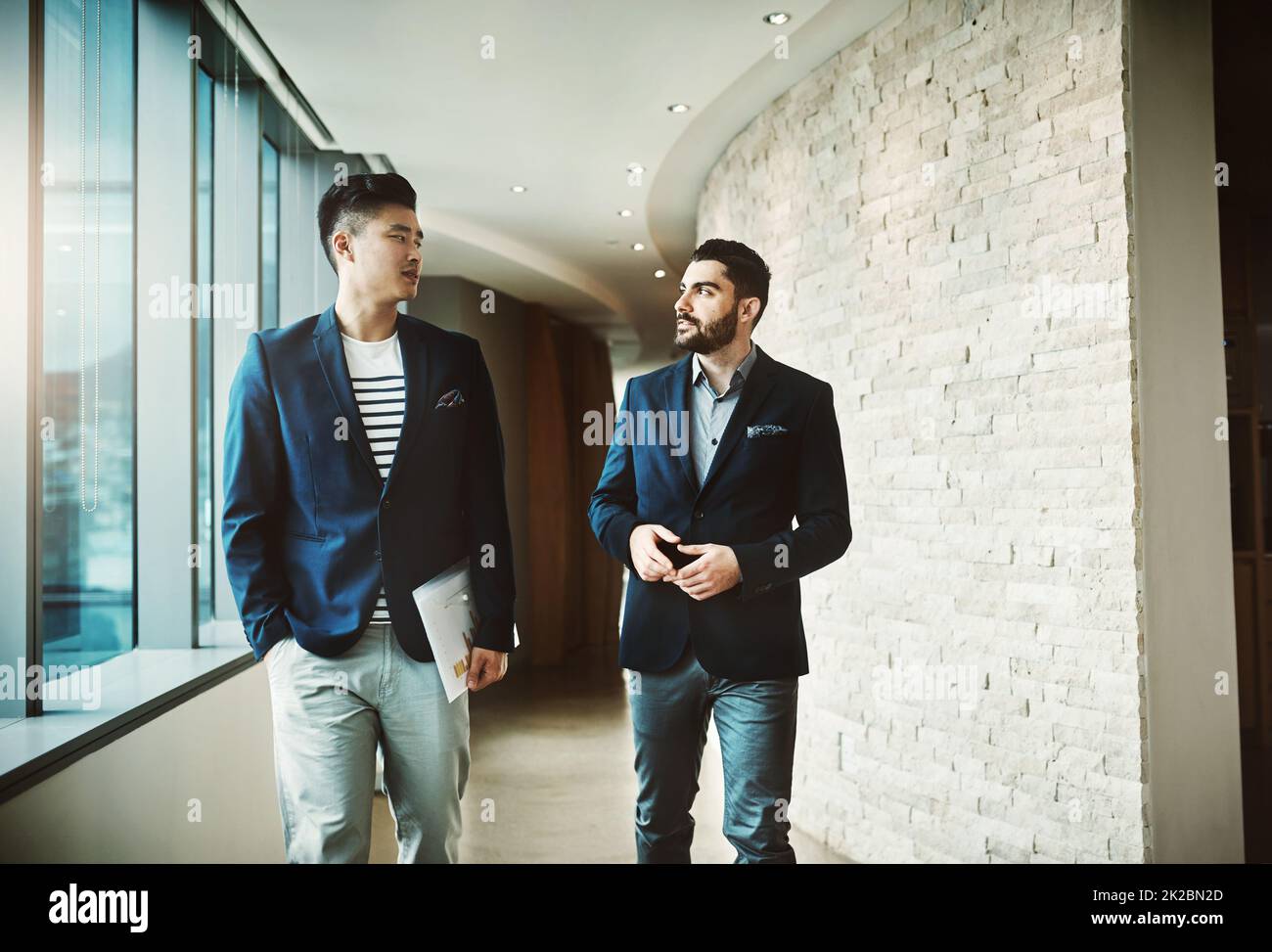 Success is all about the nows and tomorrows. Shot of two young businessmen walking and talking in a modern office. Stock Photo