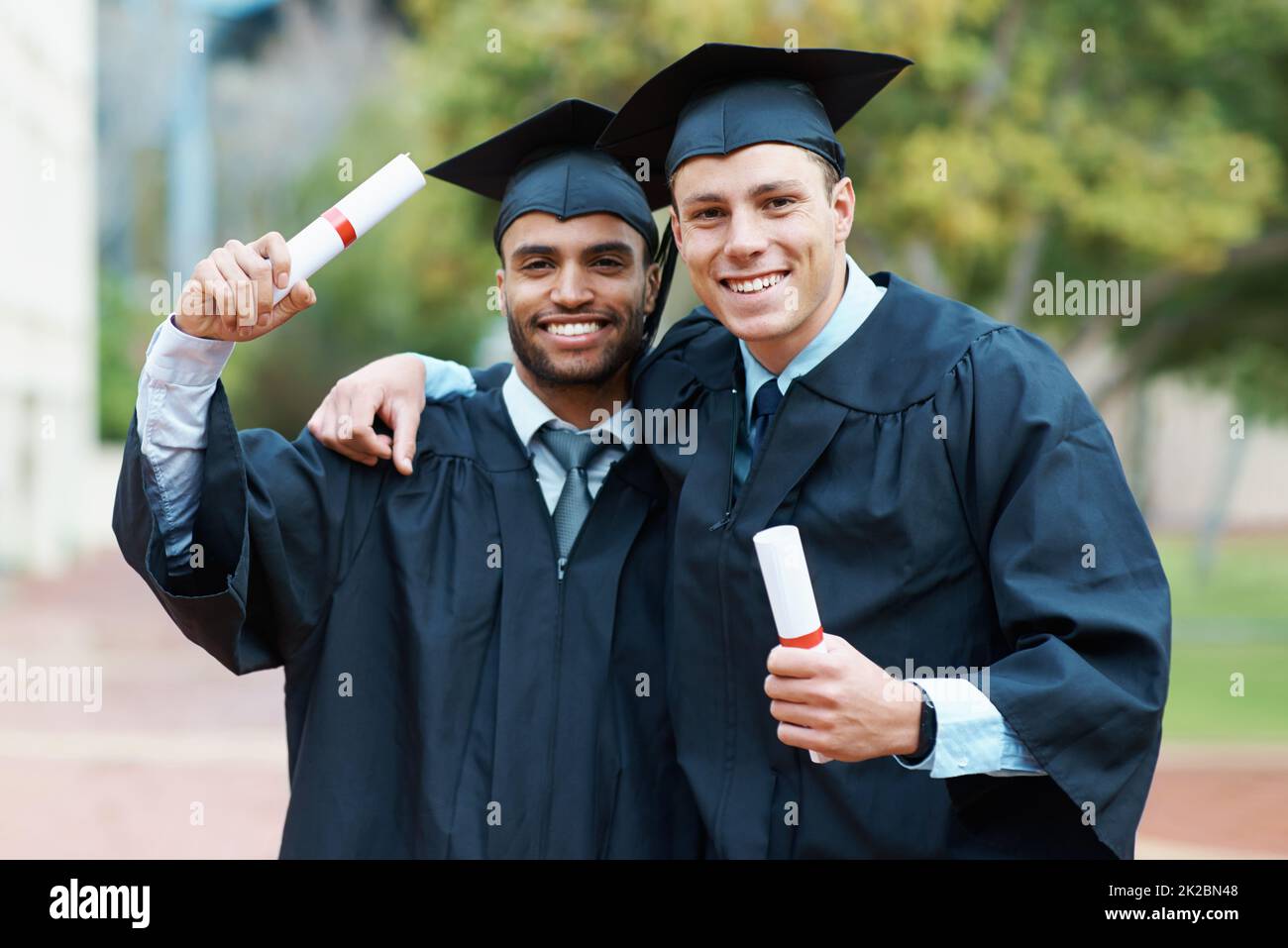 Were on our way to success. Two young college graduates holding their diplomas while wearing cap and gown. Stock Photo