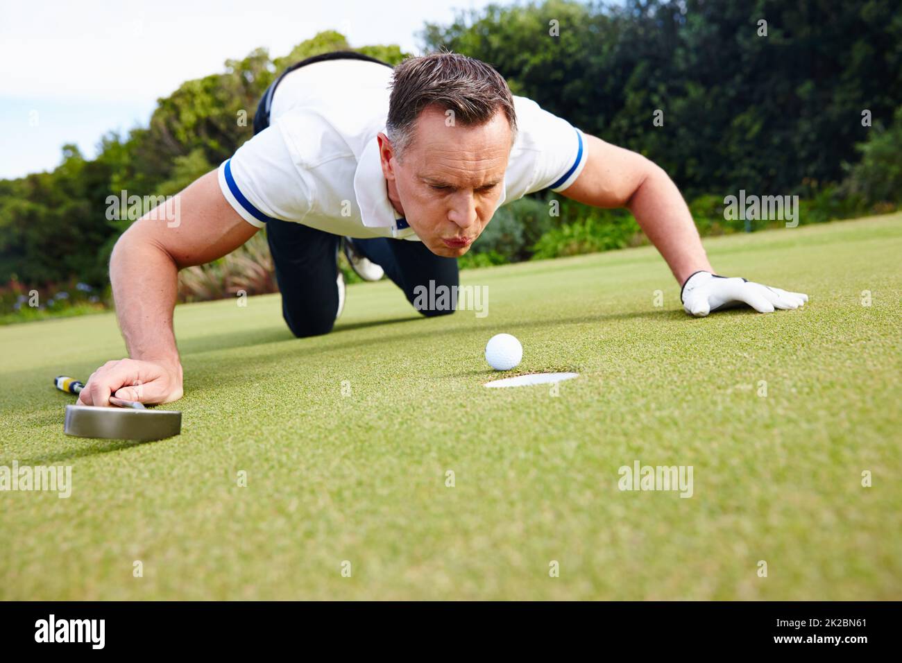 Its not cheating if nobody saw it. Shot of a handsome man trying to blow his golf ball into the hole. Stock Photo