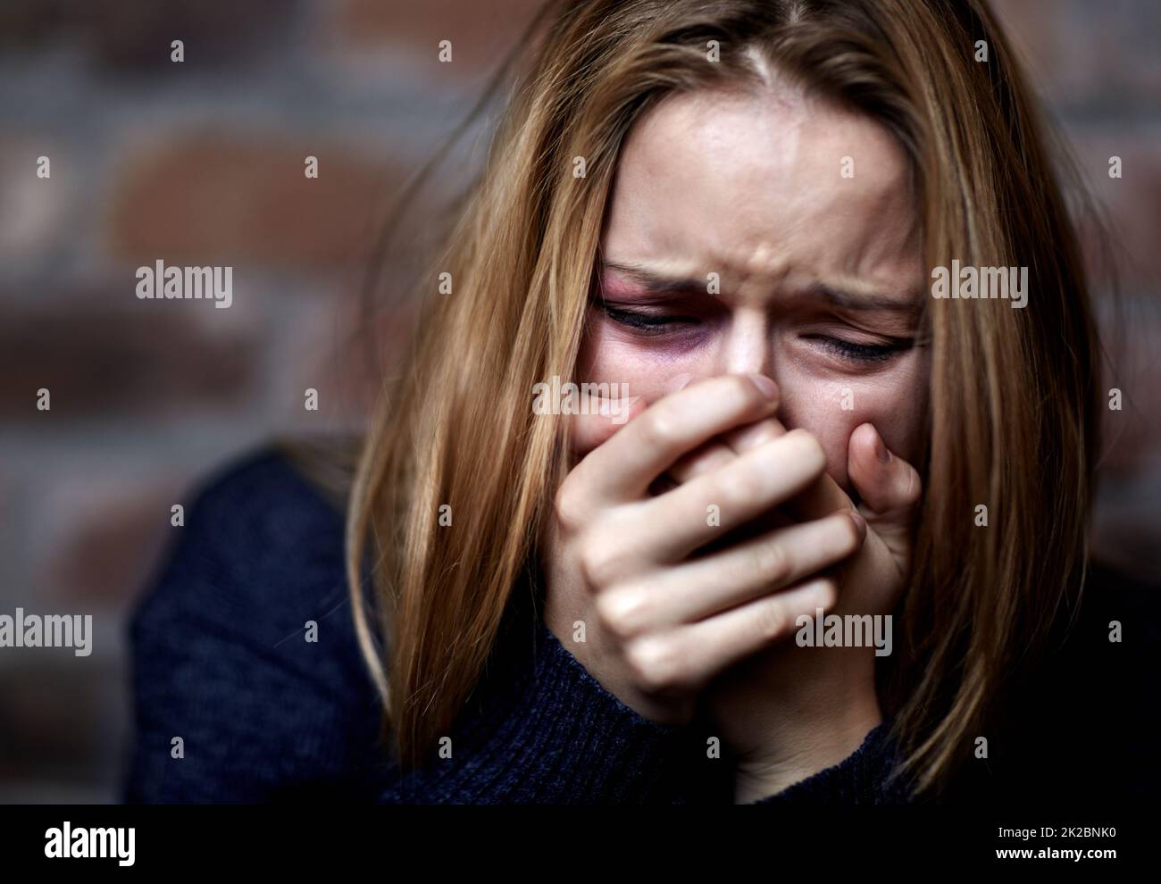 Emotionally victimized. Abused young woman crying hard and covering her mouth. Stock Photo