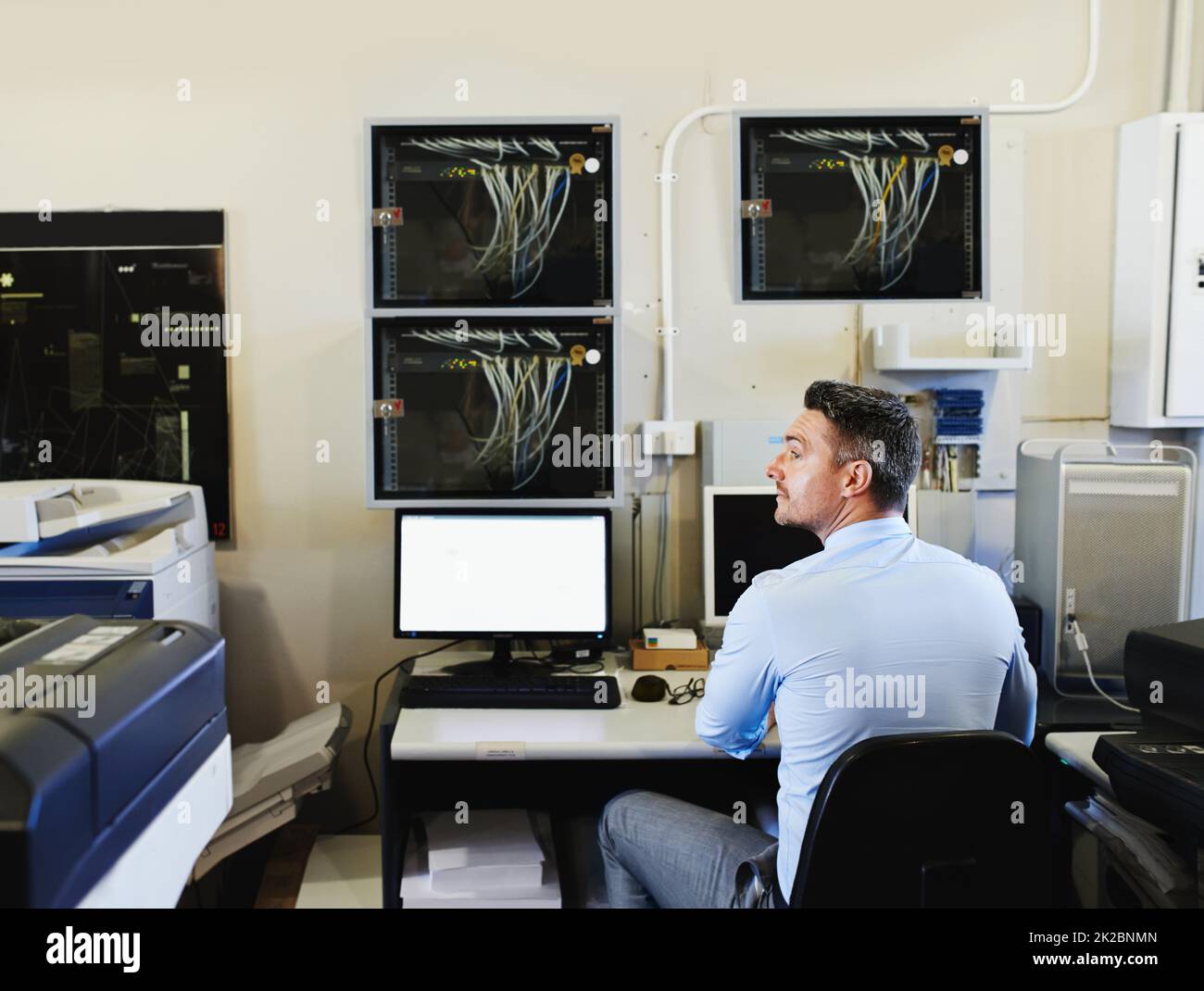 The technological heart of the company. Rearview shot of a computer engineer at work in a server room. Stock Photo