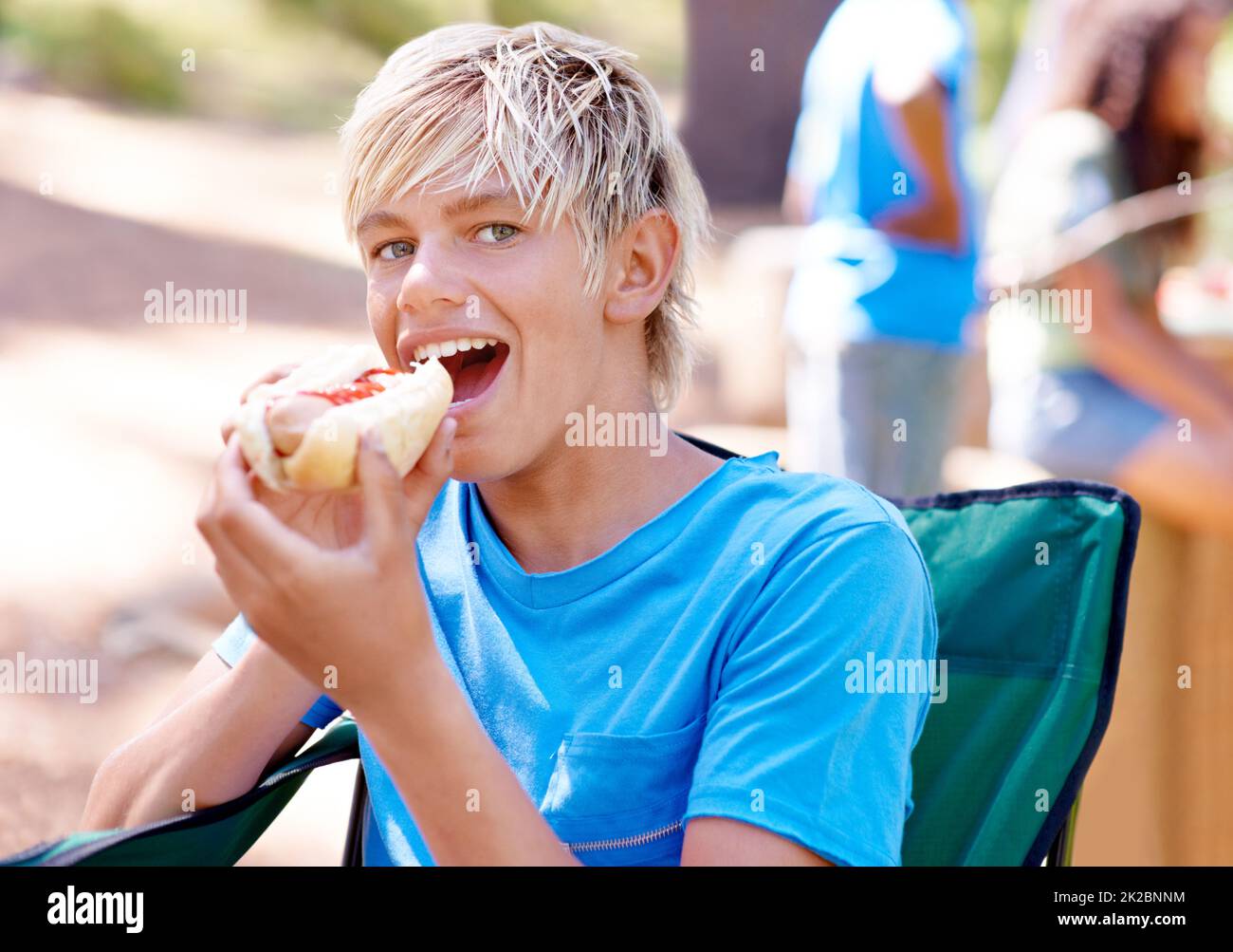 Hot dogs are my favorite. A cute little boy eating a hot dog while outdoors. Stock Photo
