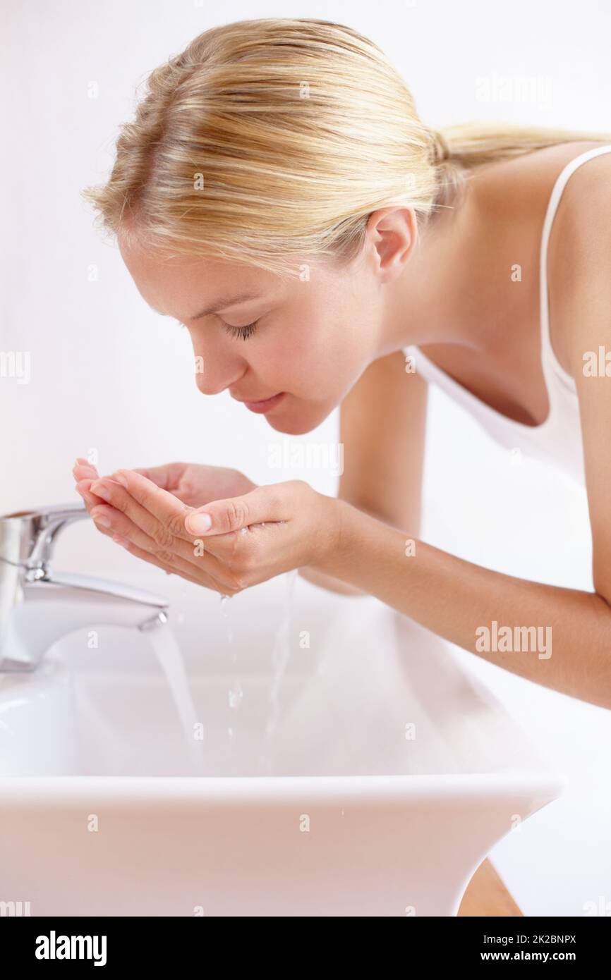 Shot of an attractive young woman washing her face with water over a
