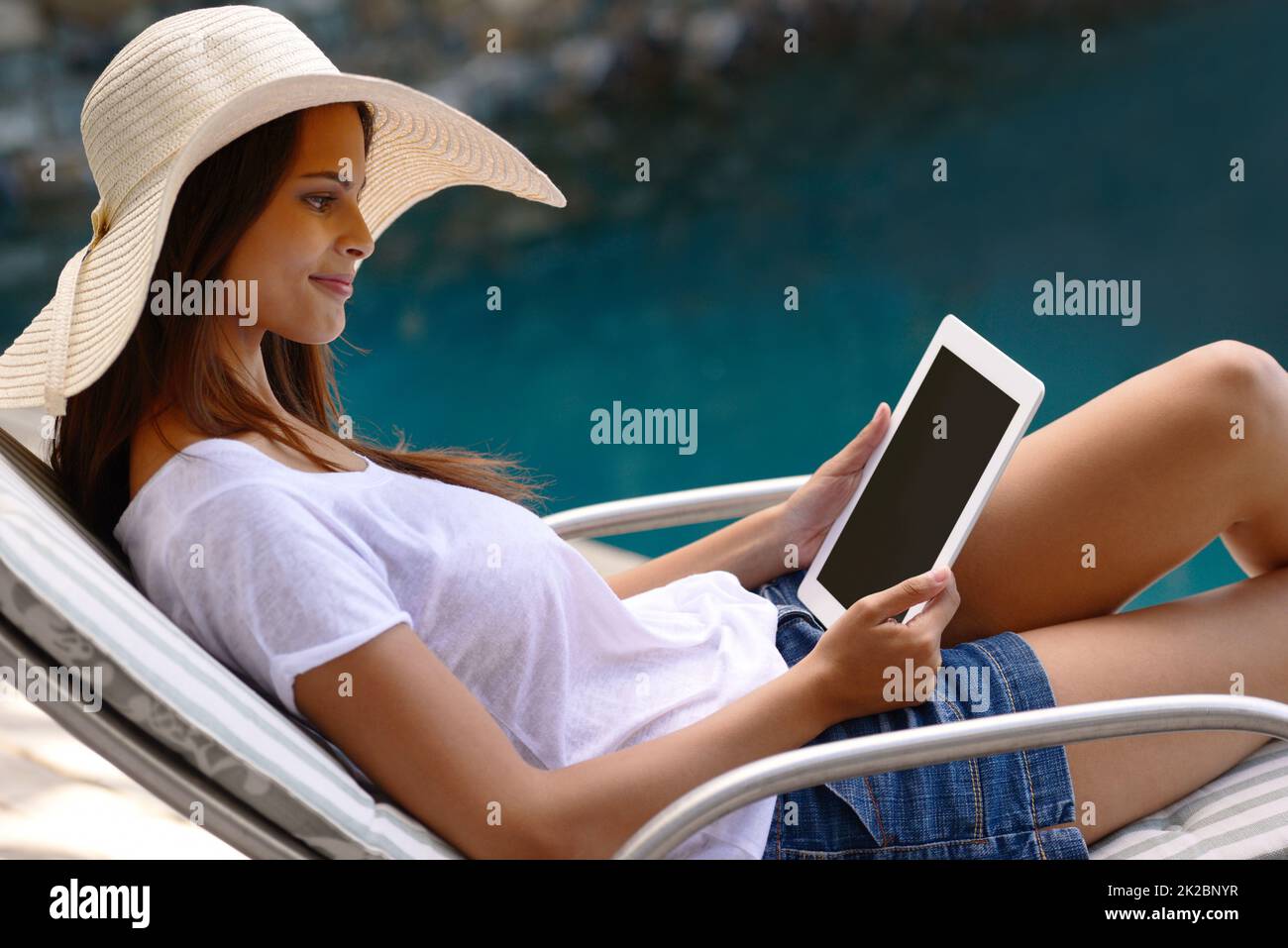 Doing some outdoor browsing. Shot of an attractive young woman using a digital tablet by the poolside. Stock Photo
