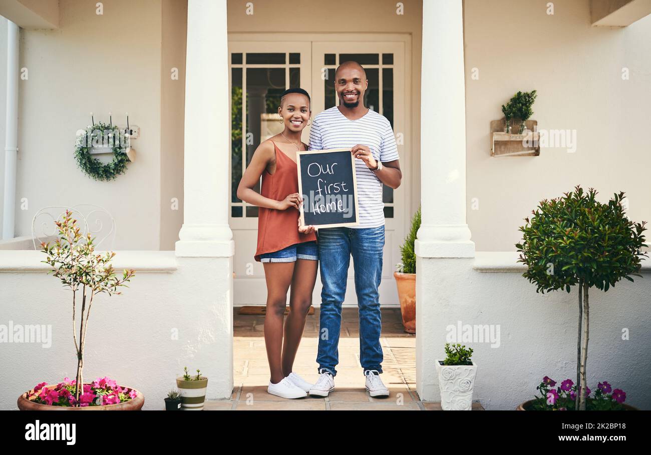 We bought our first house. Portrait of a young couple holding a chalkboard with our first home written on it. Stock Photo