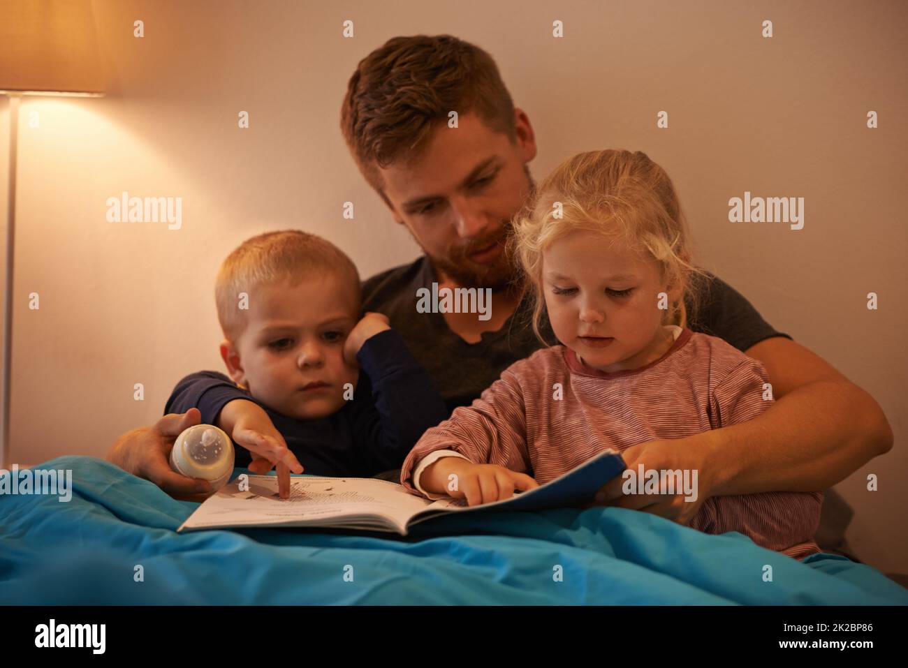 Whats that, Daddy. A father reading a bedtime story to his kids. Stock Photo