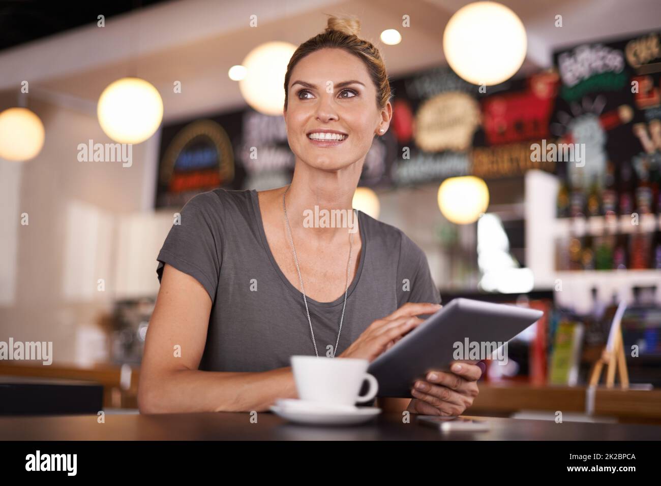 My weather app was right - its a beautiful day. A beautiful young woman using her tablet at a coffee shop. Stock Photo